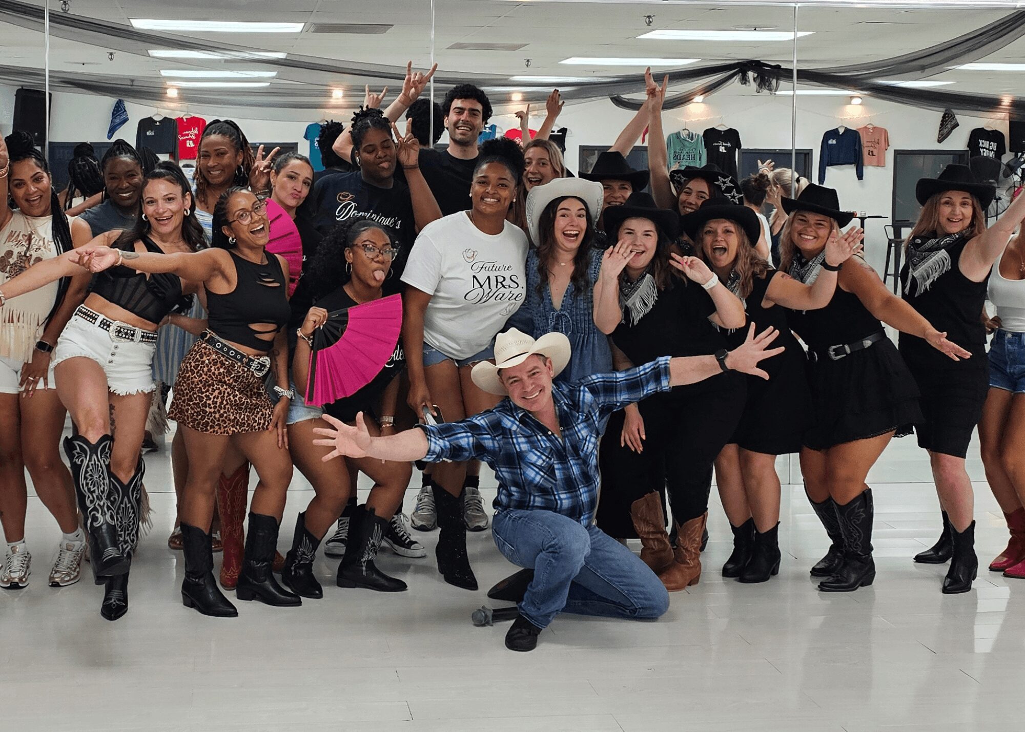 Group of people dancing indoors, some wearing cowboy hats and boots, smiling and celebrating together.