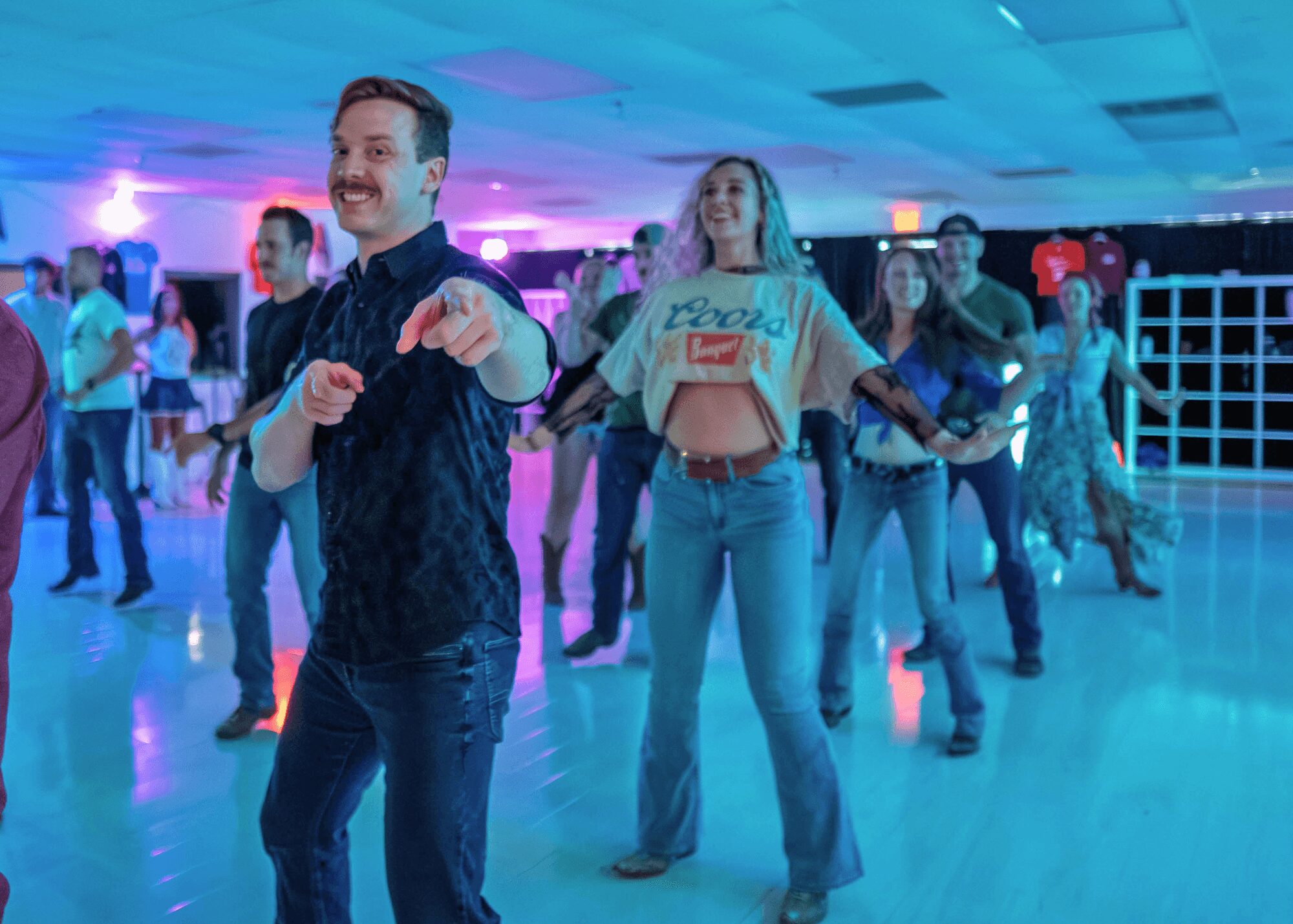 People dancing in a brightly lit indoor space with colorful lighting, smiling and enjoying music.