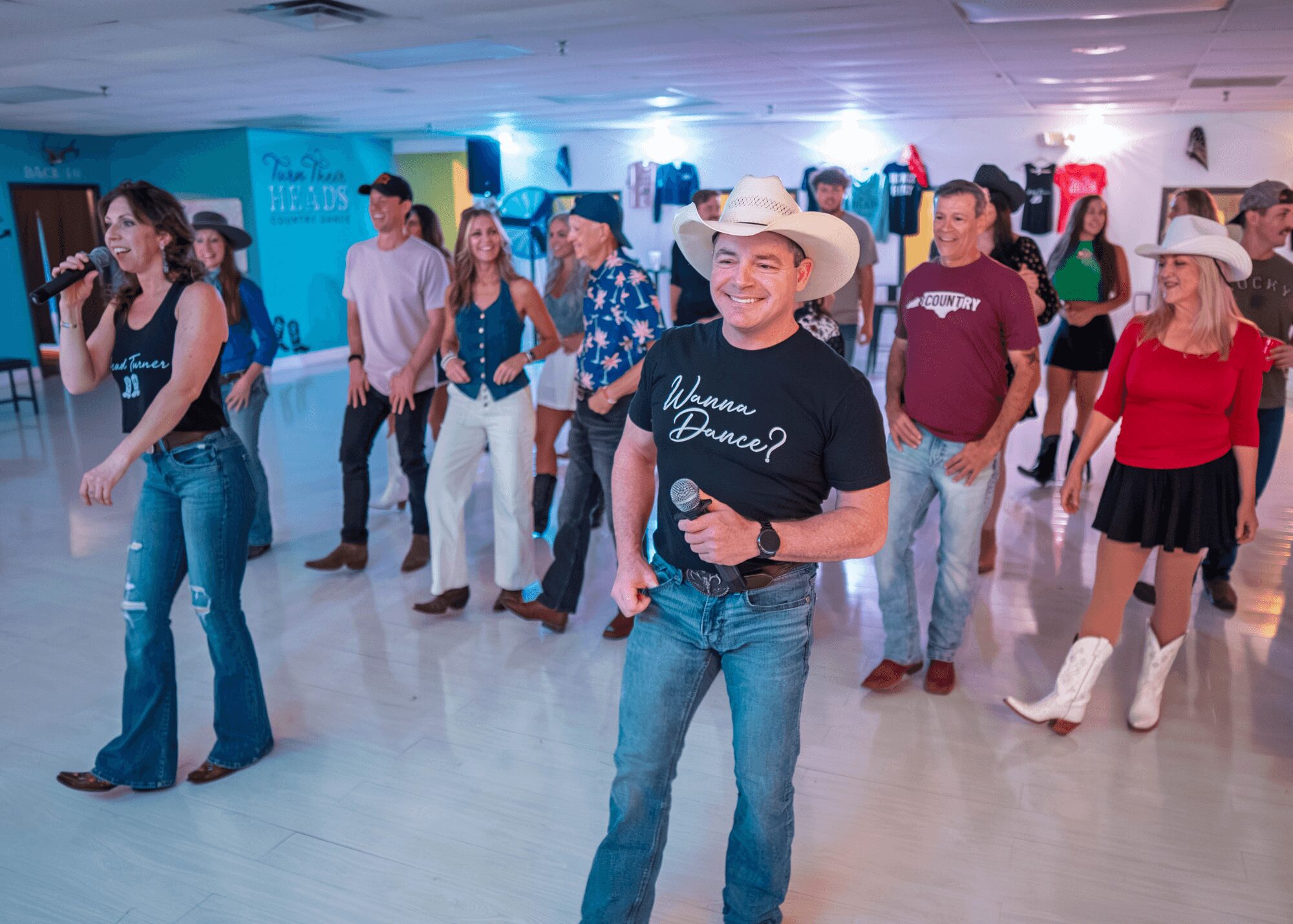 Group of people dancing in a room with colorful decorations, some wearing cowboy hats and casual clothing.