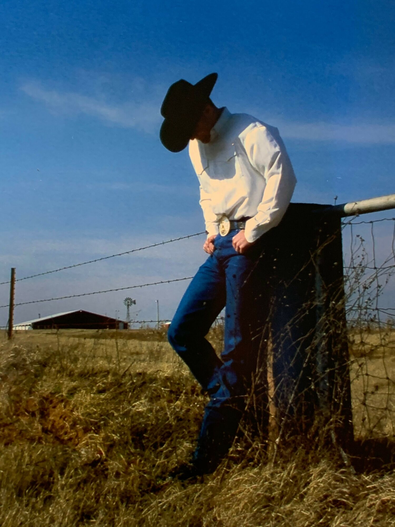 Person in white jacket and black hat leaning against a wall outdoors, holding hands with another person in blue jeans, sunny day.