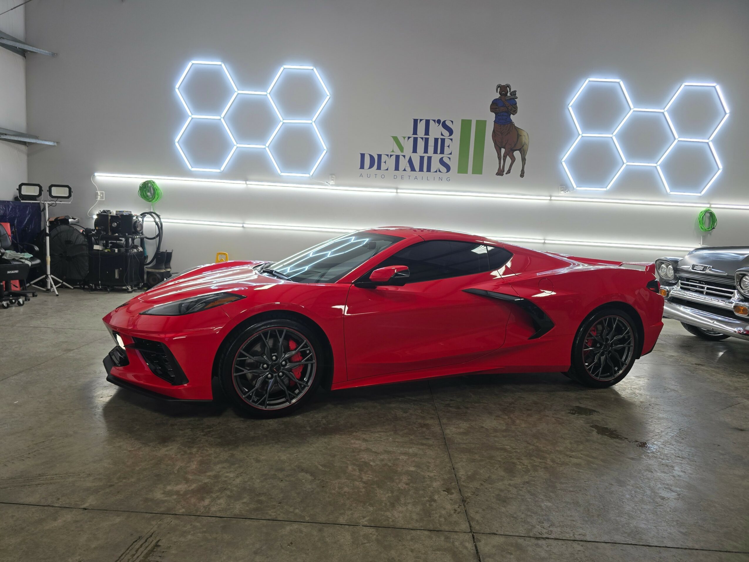 Red sports car parked indoors with hexagonal light fixtures on the wall behind it.