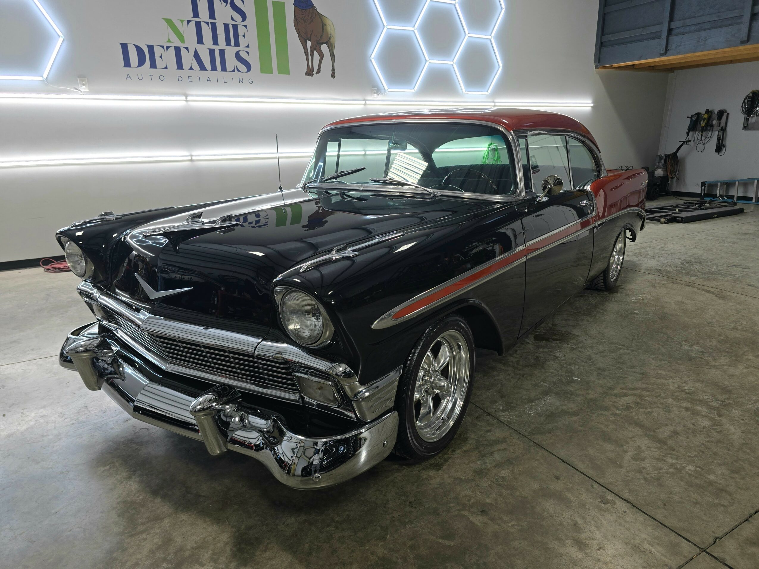 Black vintage car with chrome details parked indoors, with a red roof and a hexagonal wall pattern in the background.
