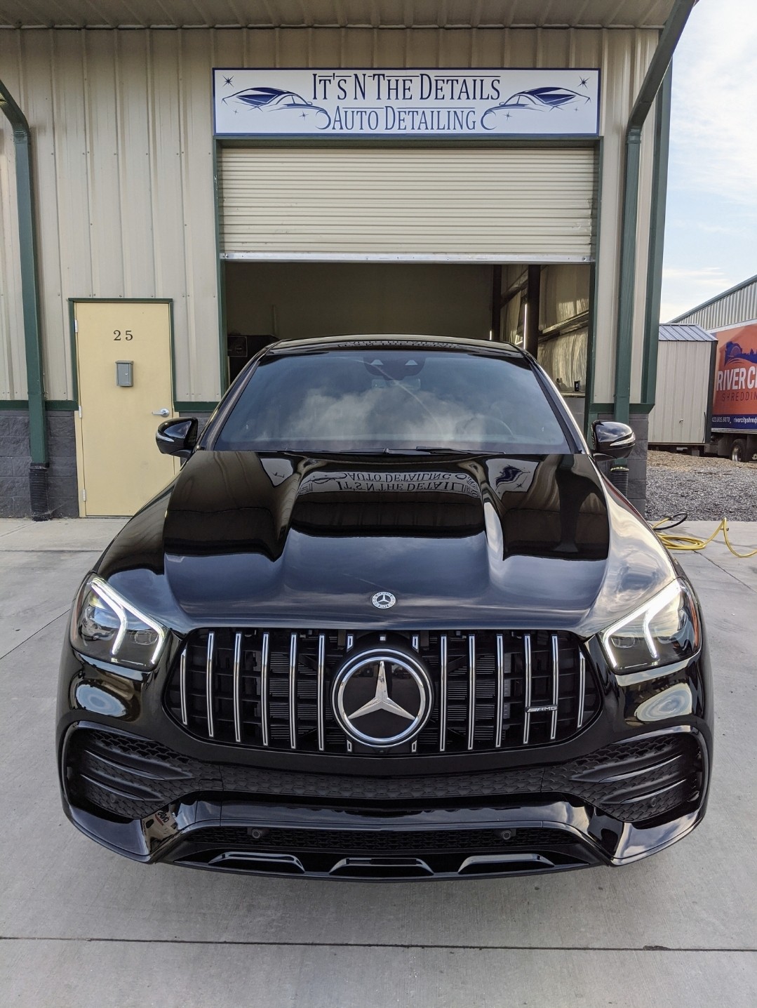 Black Mercedes-Benz car parked outside an auto detailing shop with a sign reading 'It's in the Details Auto Detailing'.