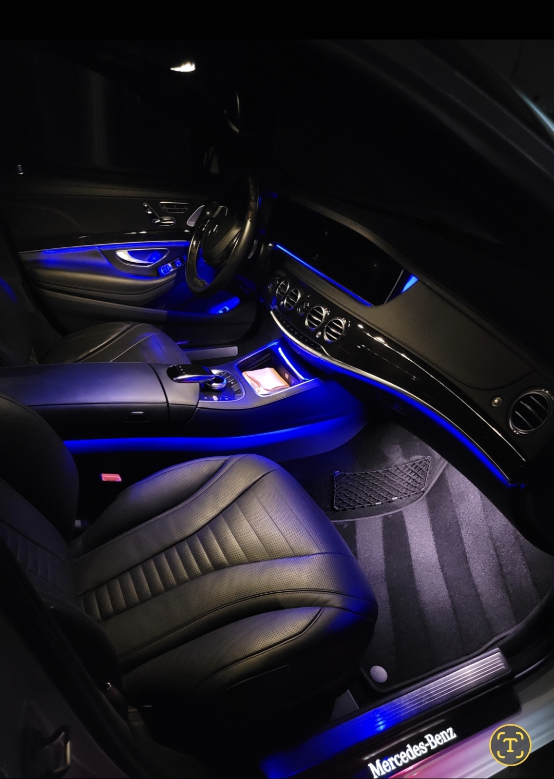 Car interior illuminated with blue lights, showing a leather seat, dashboard, and steering wheel.