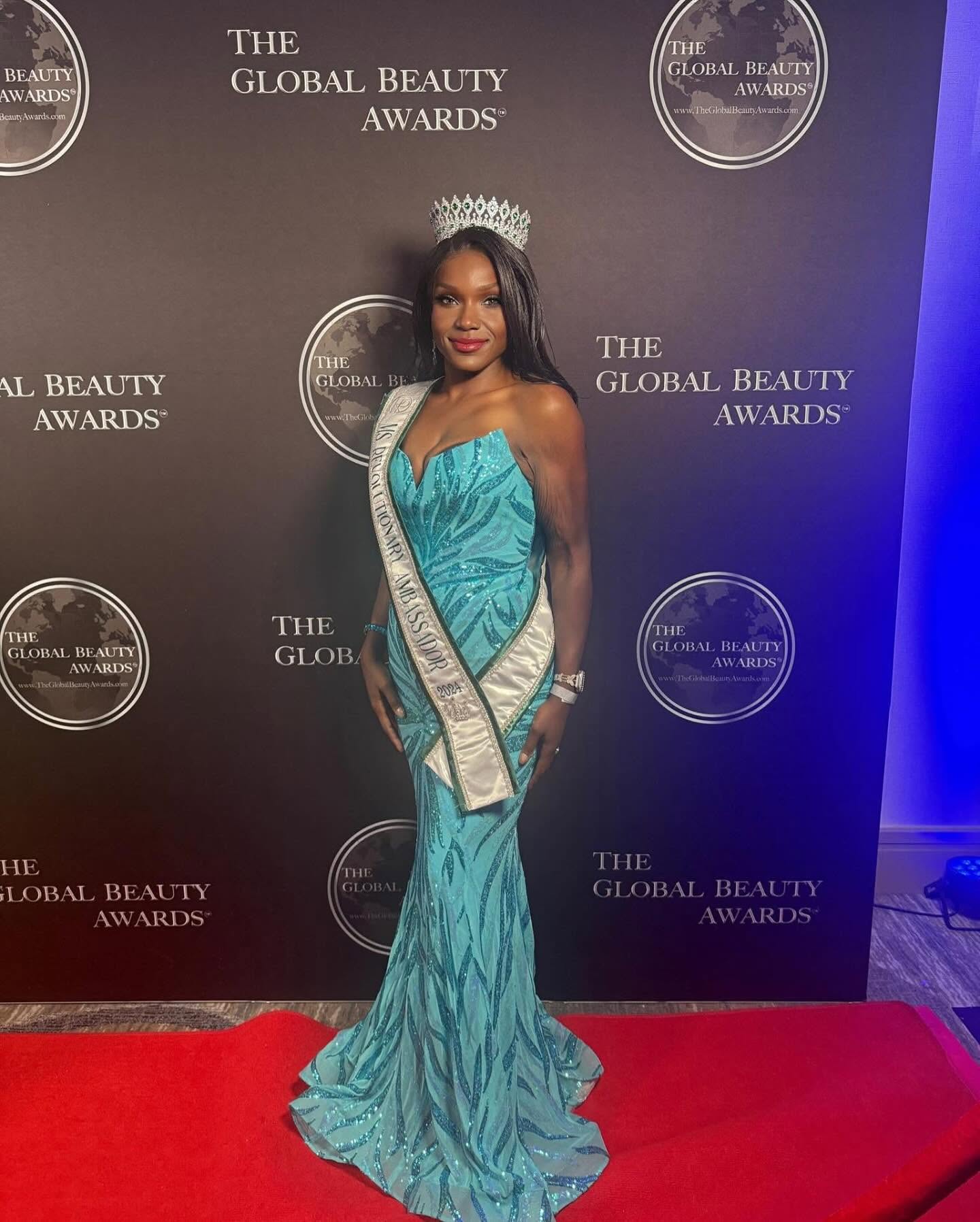 Woman in a turquoise gown with a sash and crown, standing on a red carpet at the Global Beauty Awards, smiling.