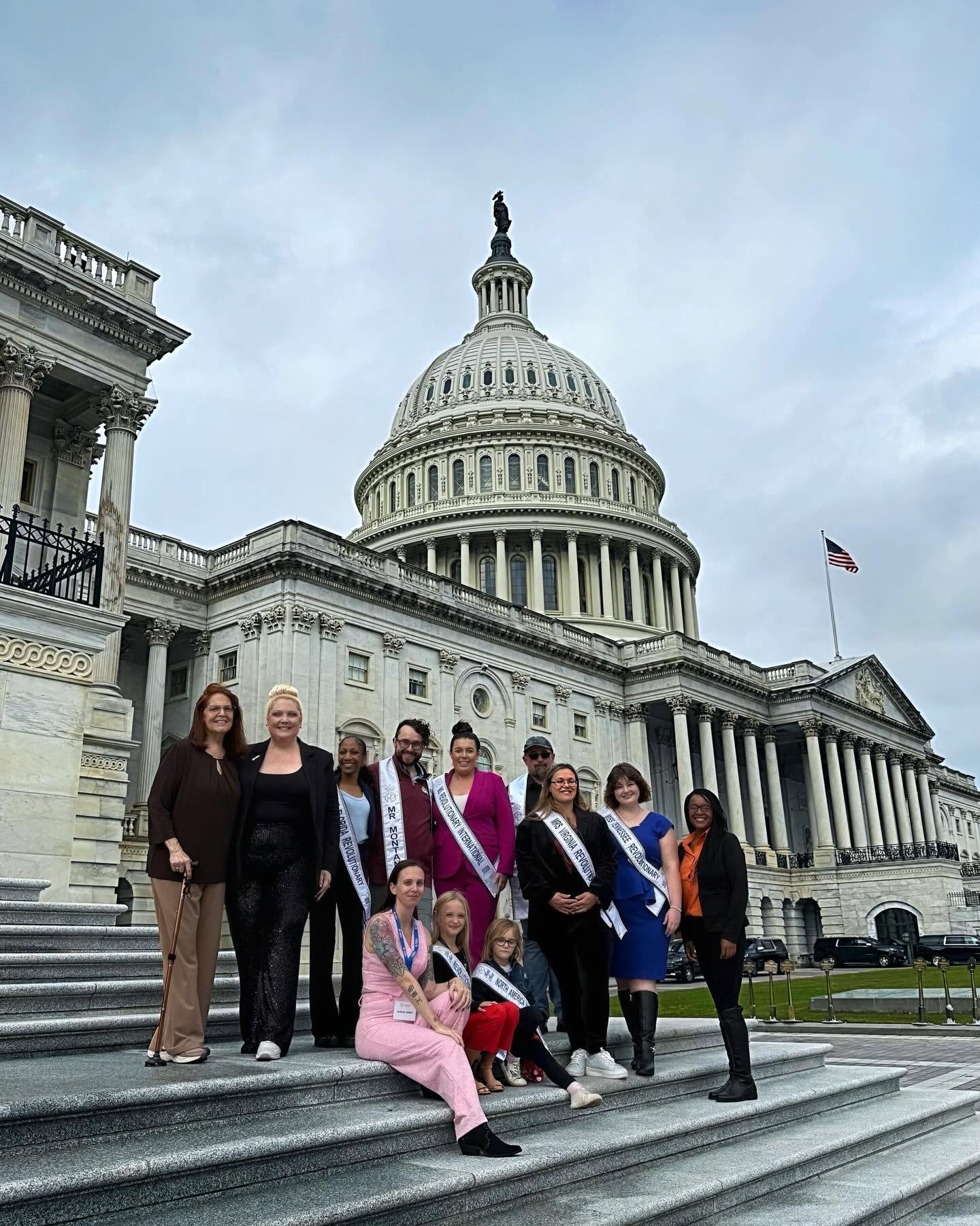 Group of women standing on steps in front of the U.S. Capitol building, some wearing sashes, under cloudy sky.