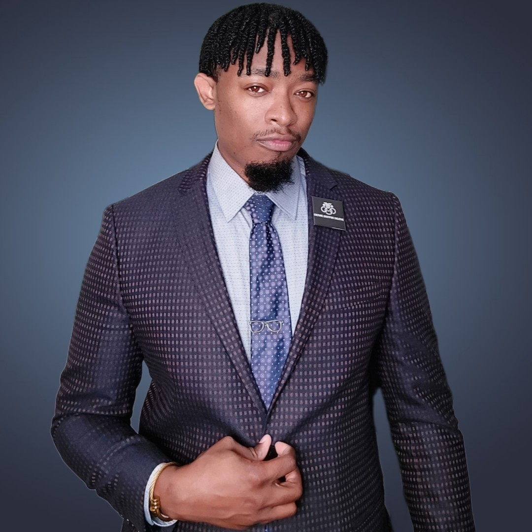 Man in a checkered suit with a tie, standing against a dark background.