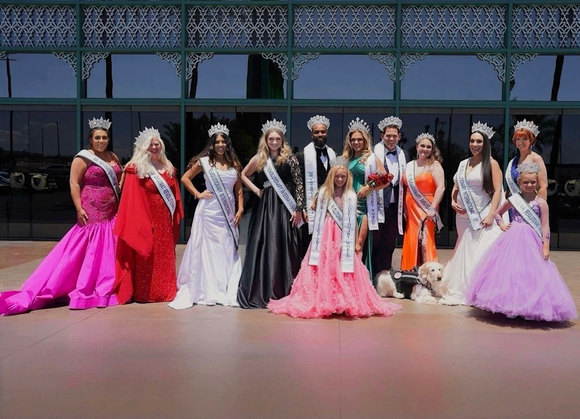 Group of women in colorful gowns and crowns standing outdoors on a stage, with a building in the background.