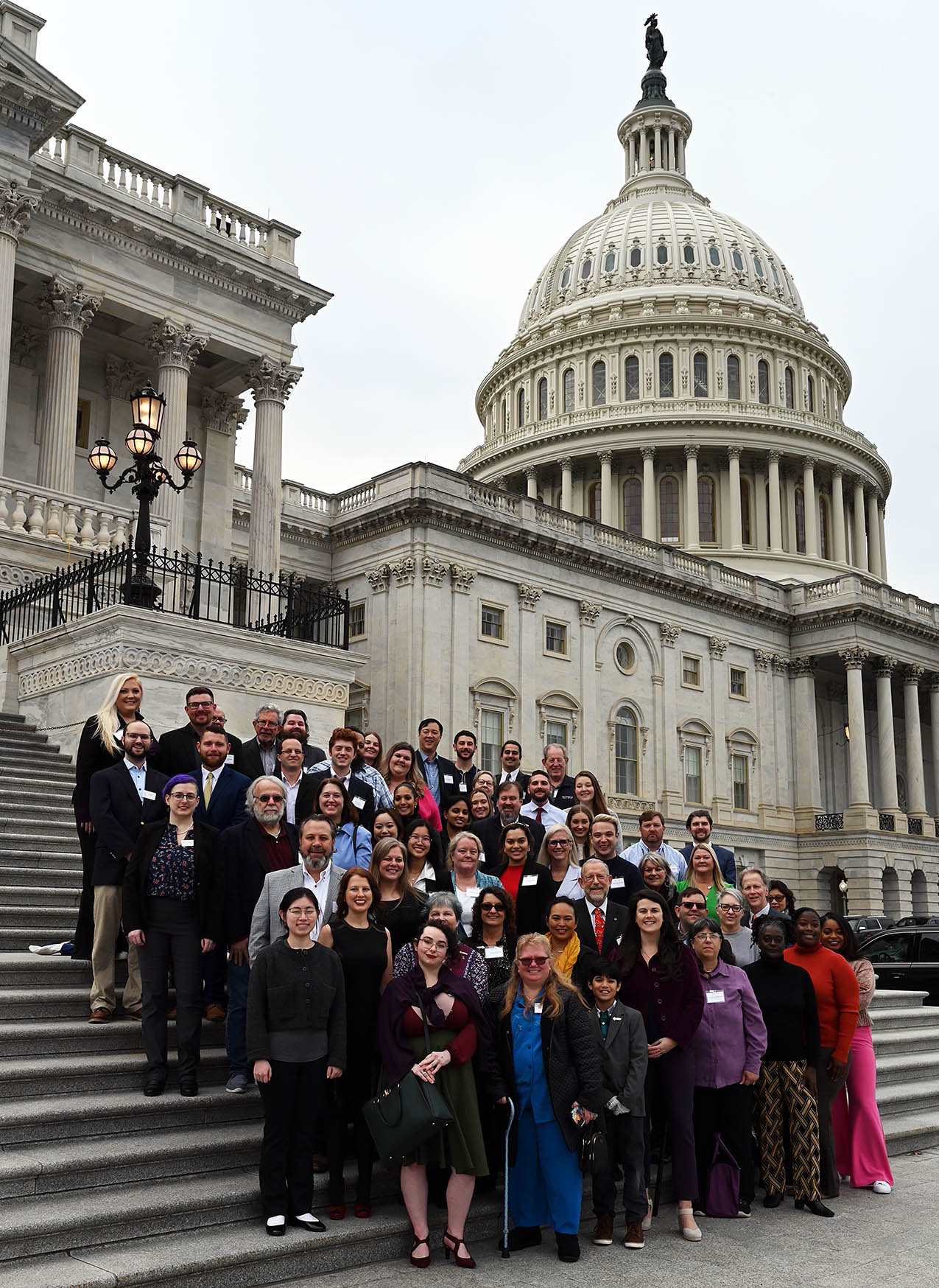 Group of people standing on steps in front of the U.S. Capitol building with a large dome and columns.