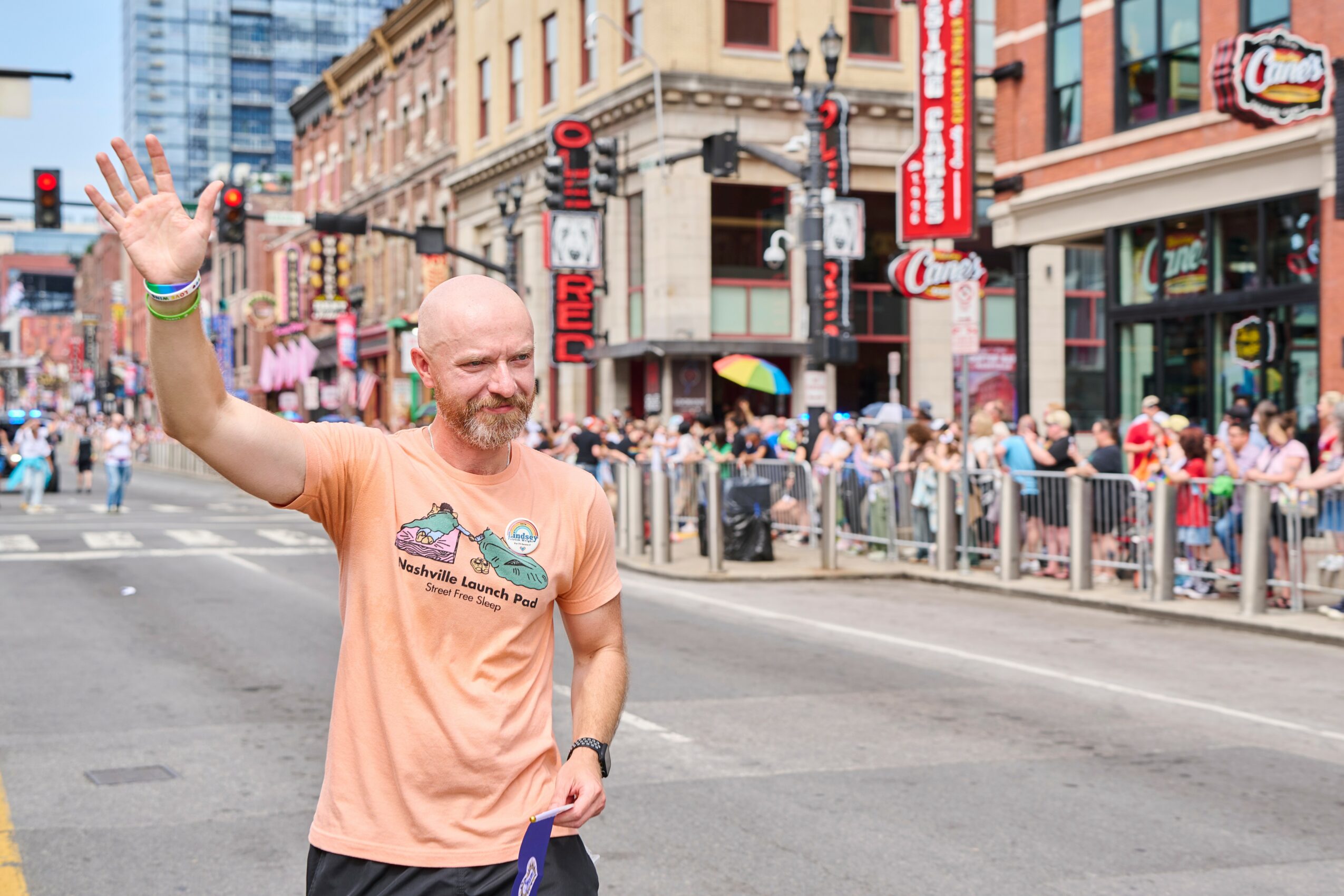 Man waving on city street with crowd and buildings in background