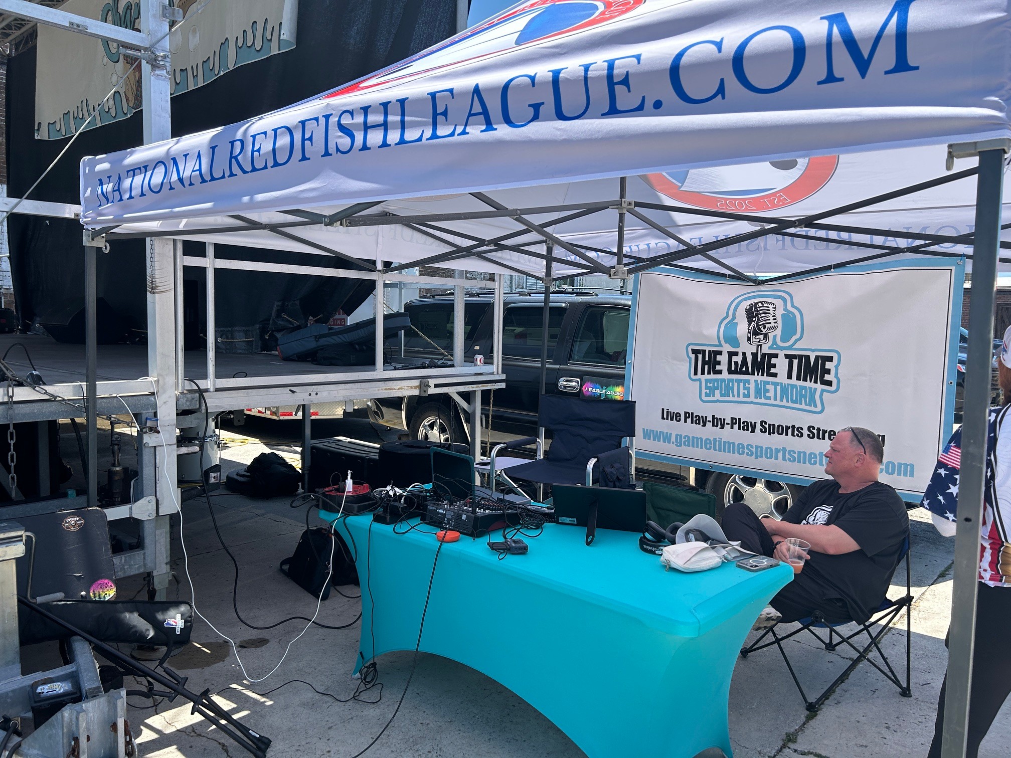 Person sitting at a table under a tent with a banner for the Red Fish League, with electronic equipment on the table.