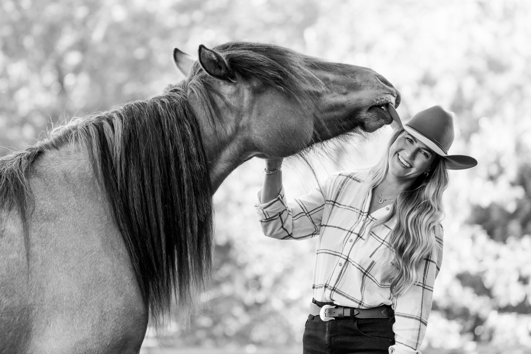 Woman with long hair and cowboy hat petting a horse's face outdoors, smiling, in black and white.
