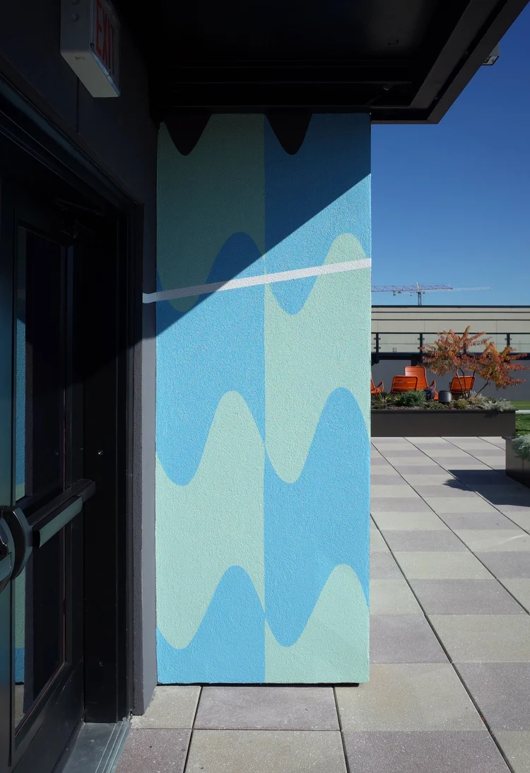 Colorful wall with blue and green abstract shapes outside a building, with a clear sky and outdoor area visible.