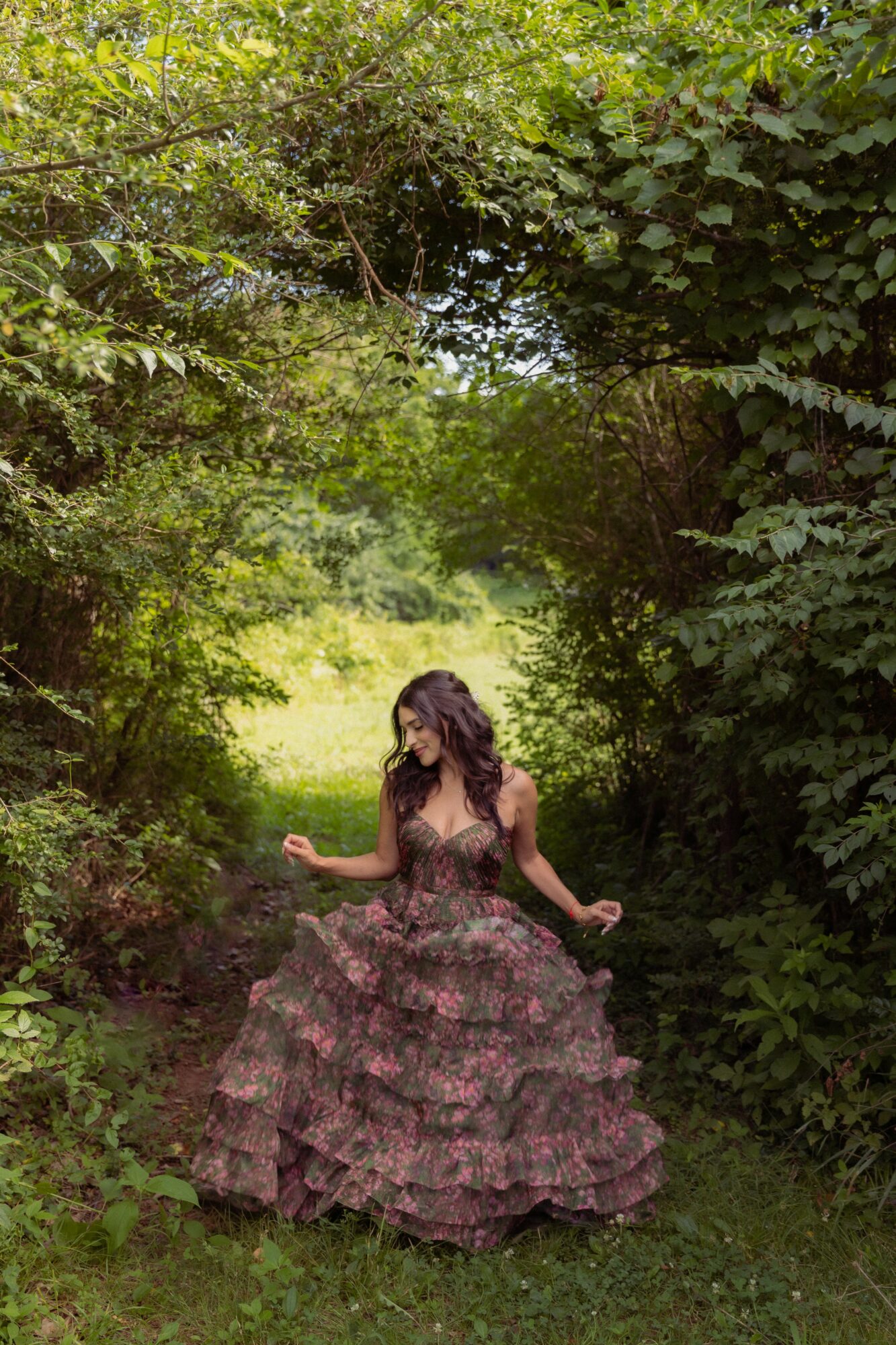 Woman in a long, floral dress standing in a lush green forest clearing.