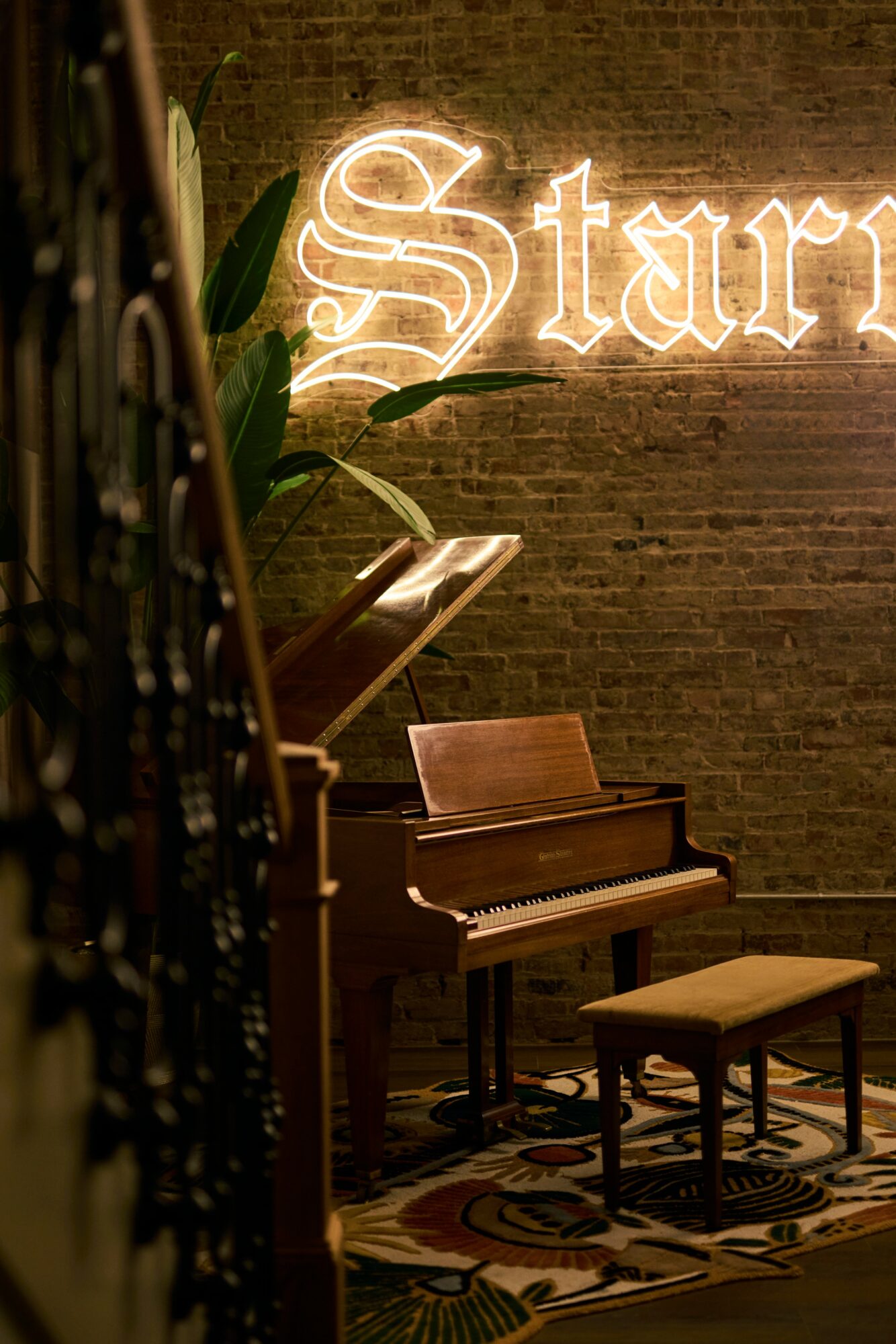 Piano with bench in front of a brick wall with a neon sign reading 'Star'.