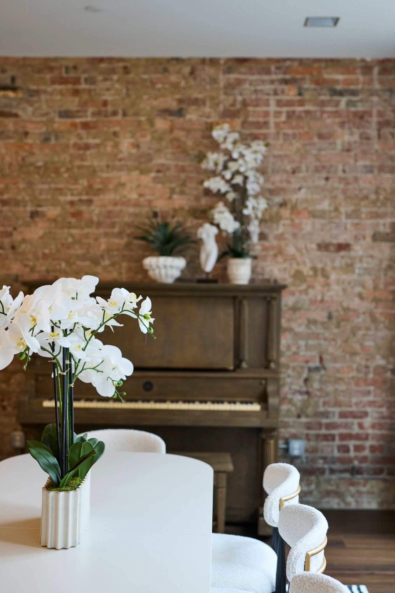 White orchid in a pot on a table, brick wall background with a piano and decorative vases, minimalistic interior.