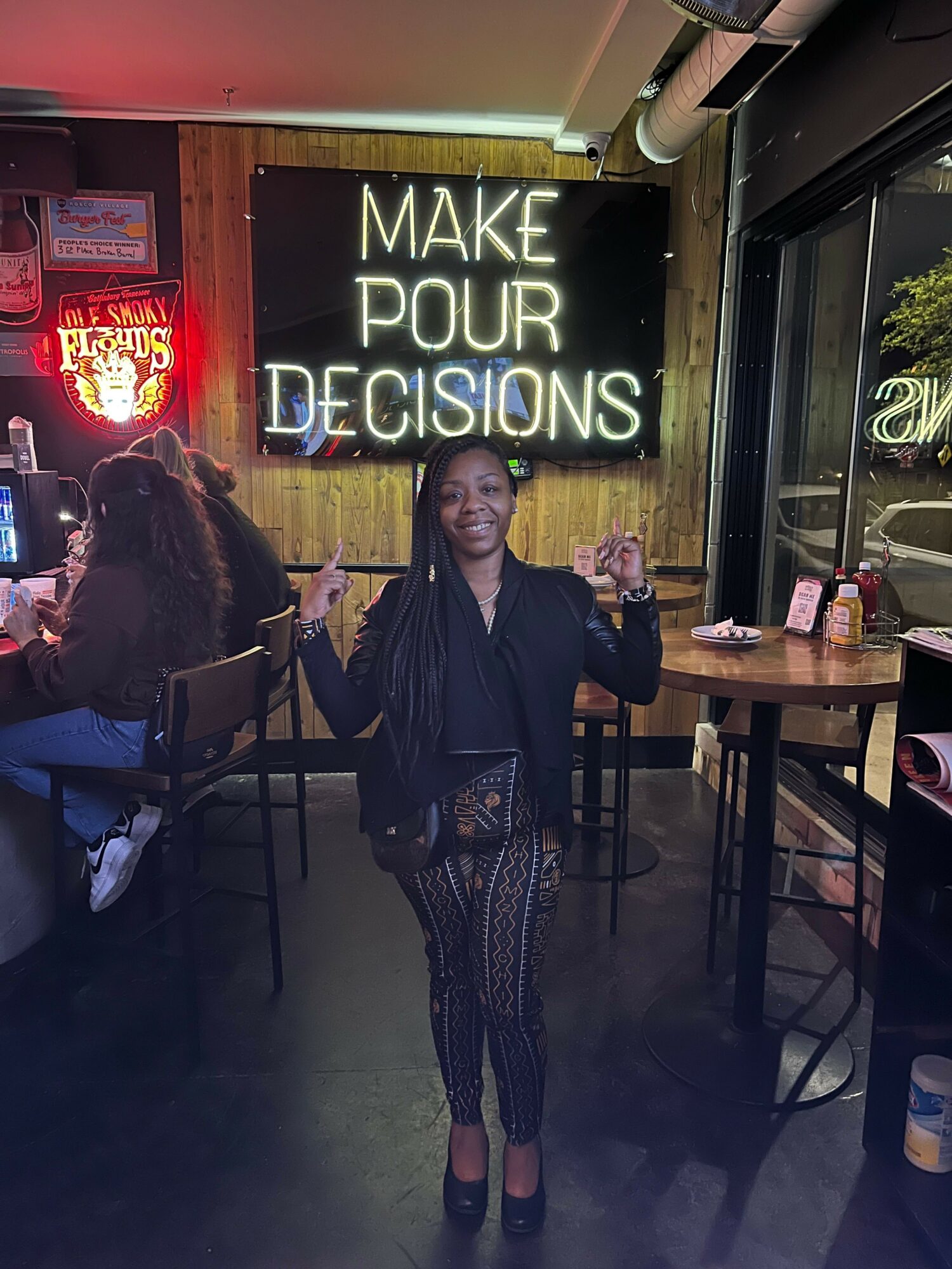 Person standing in front of a sign that reads 'MAKES POUR OUR DECISIONS' inside a dimly lit venue.