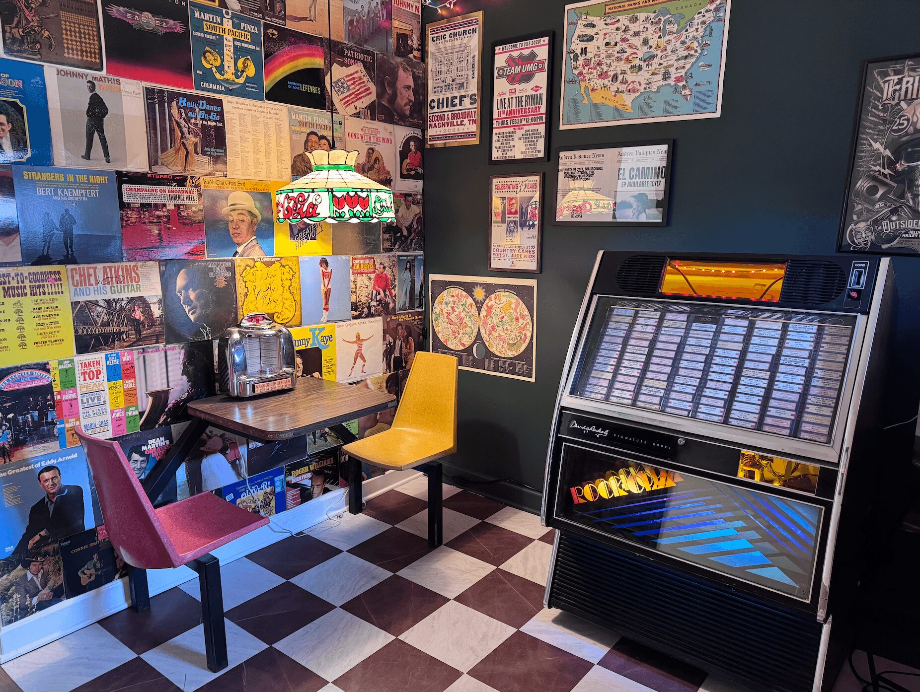 Room with colorful posters, a jukebox, a table with chairs, and a checkered floor.