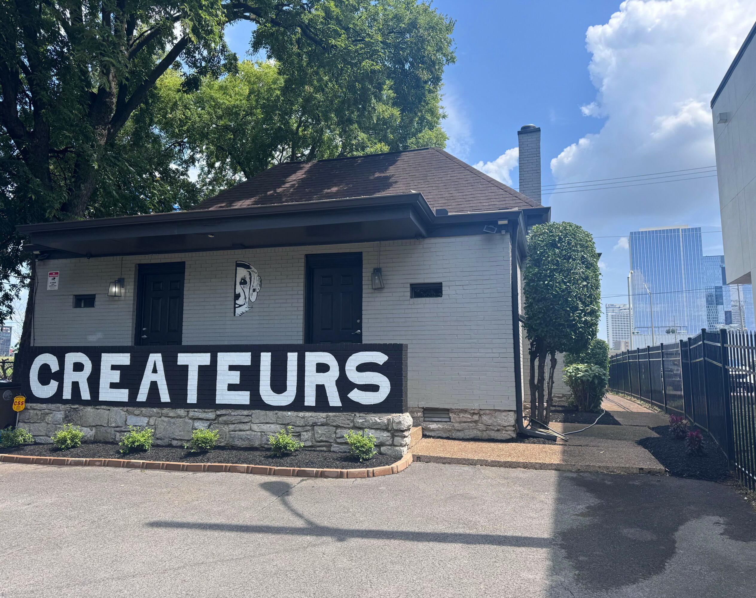 Small house with a sign reading 'CREATEURS' in front, trees and a blue sky in the background.