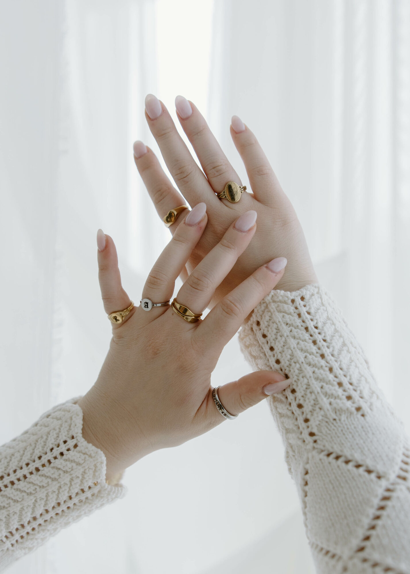 Two hands with rings, one hand resting on the other, against a light background, wearing knitted sleeves.