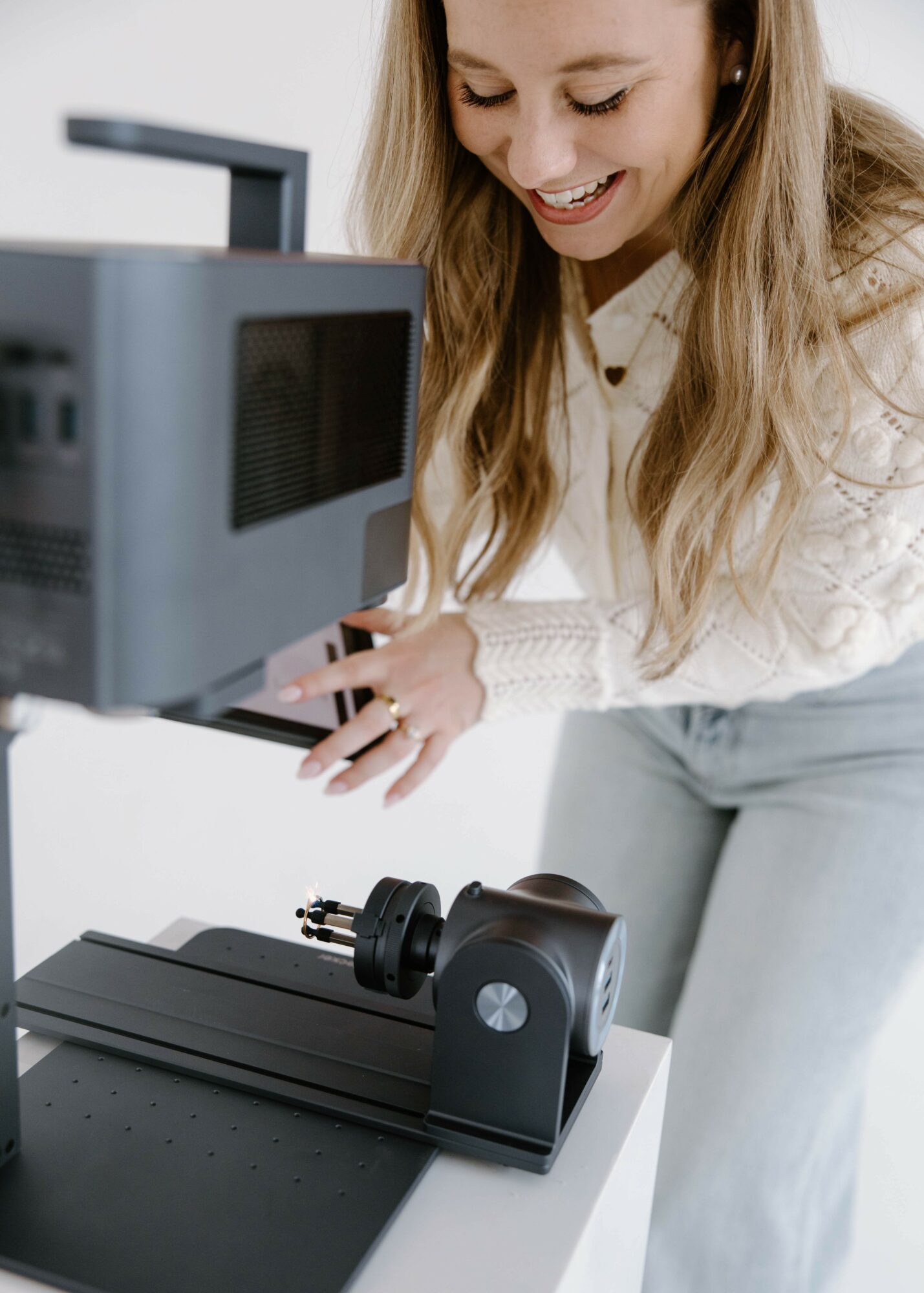 Woman smiling and looking at a computer monitor, with a device on a table in front of her.