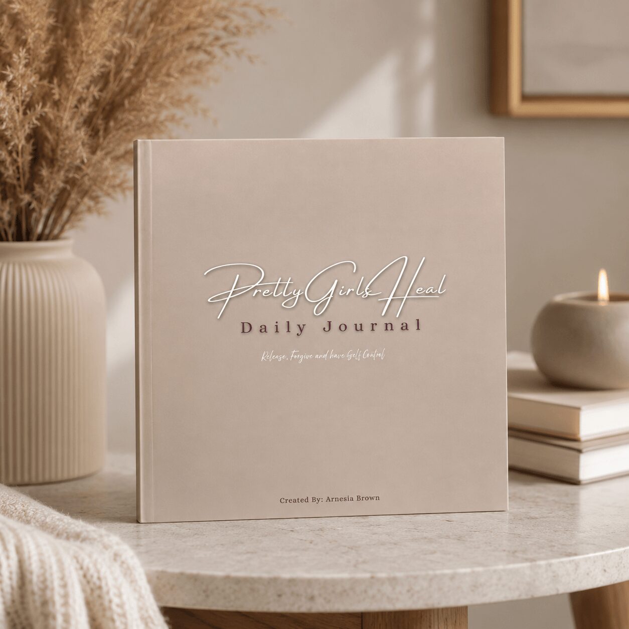 A beige journal titled 'Pretty Girl Aesthetic Daily Journal' on a table with a vase, candle, and books.