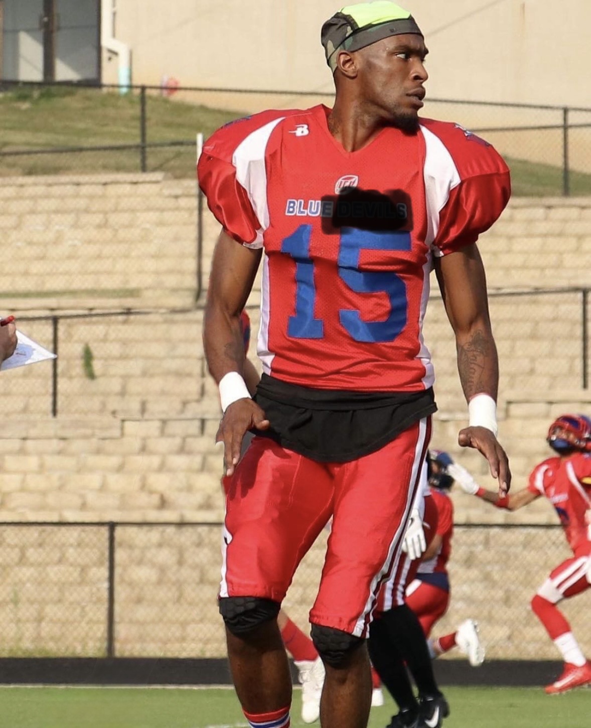 Football player in red uniform with the number 15, standing on the field during a game.