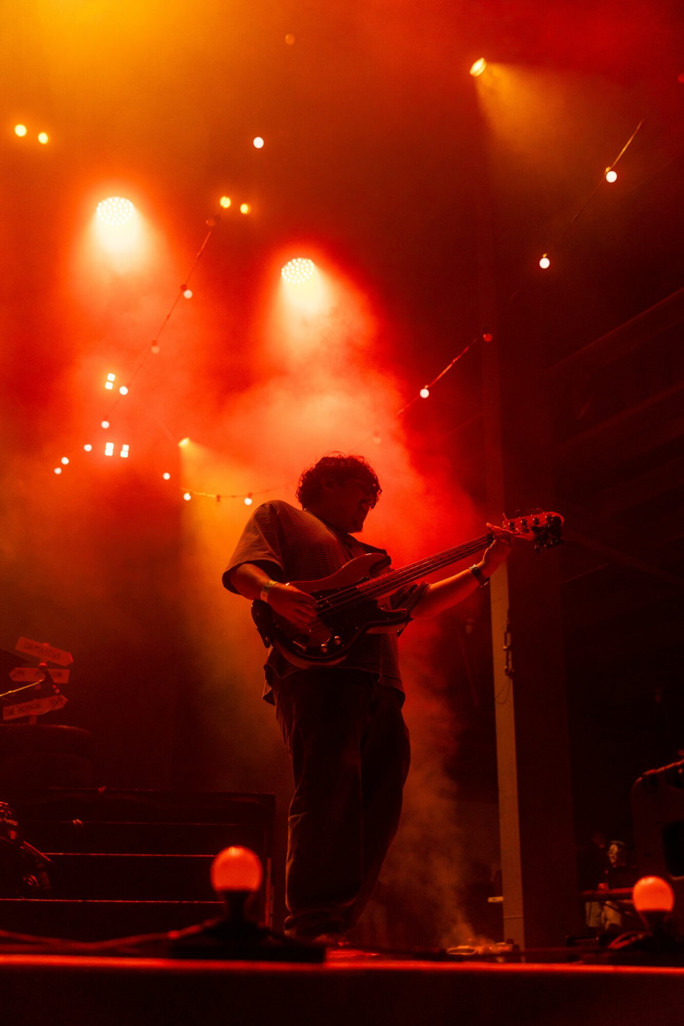 Musician playing guitar on stage with colorful lights and smoke effects, silhouette visible against vibrant background.