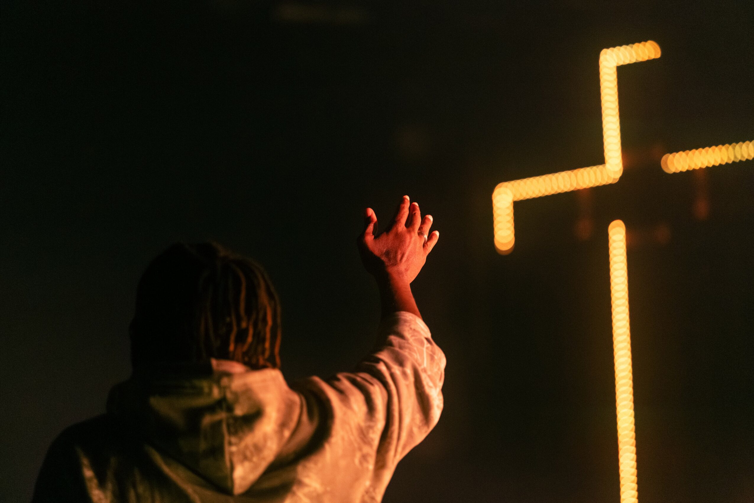 Person with raised hand facing illuminated geometric shapes in dark environment.