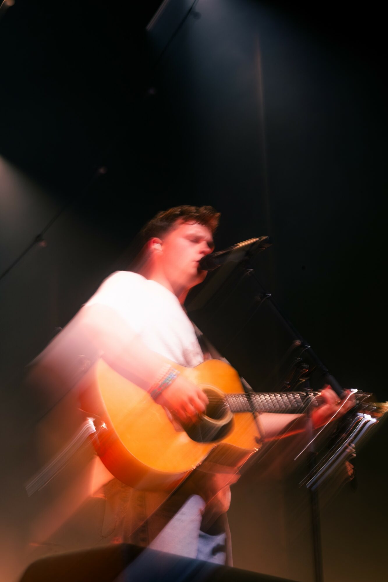 Young person playing an acoustic guitar on stage with dark background.