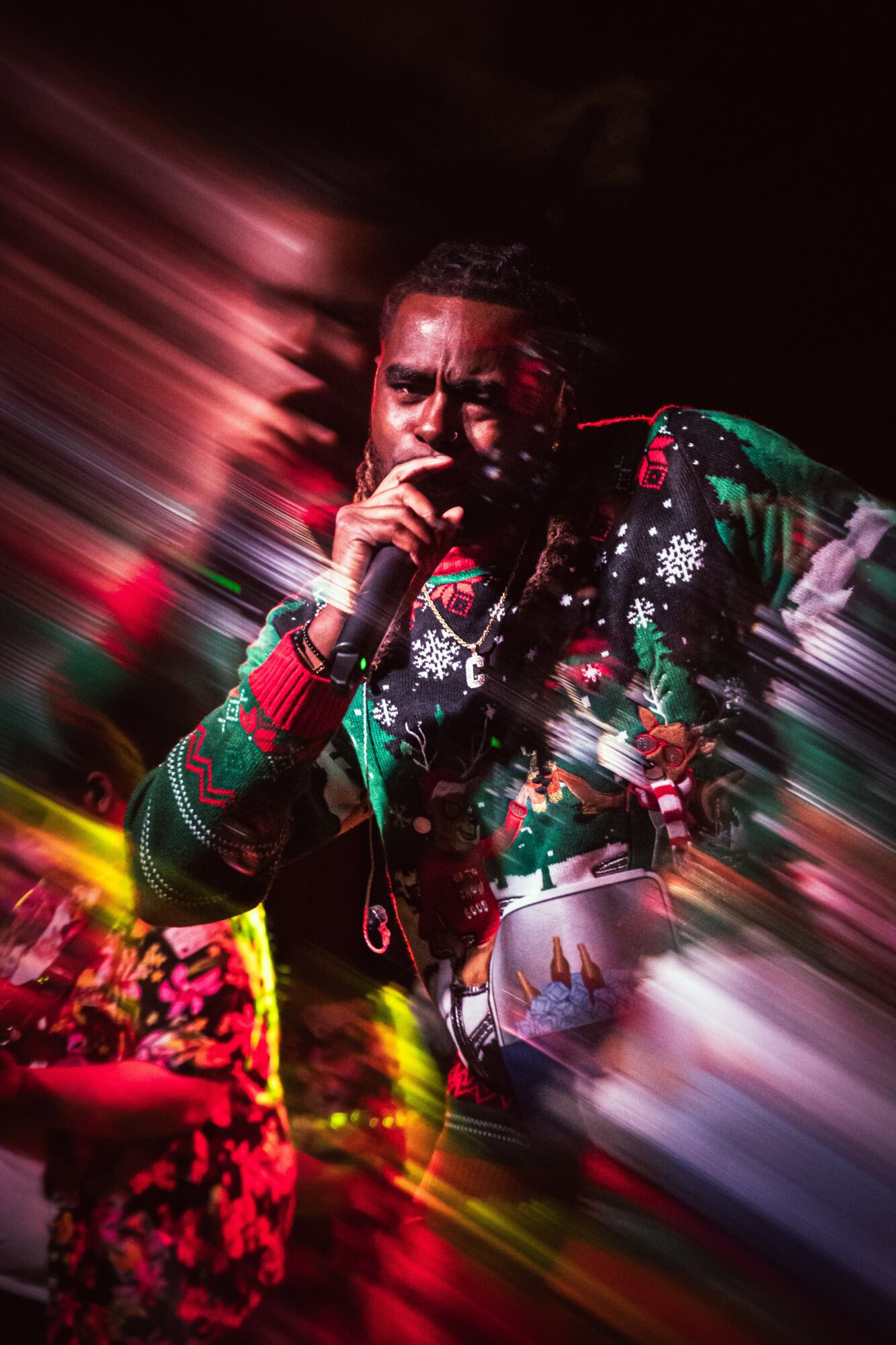 Person with hand near face, wearing colorful patterned clothing, with motion blur background.