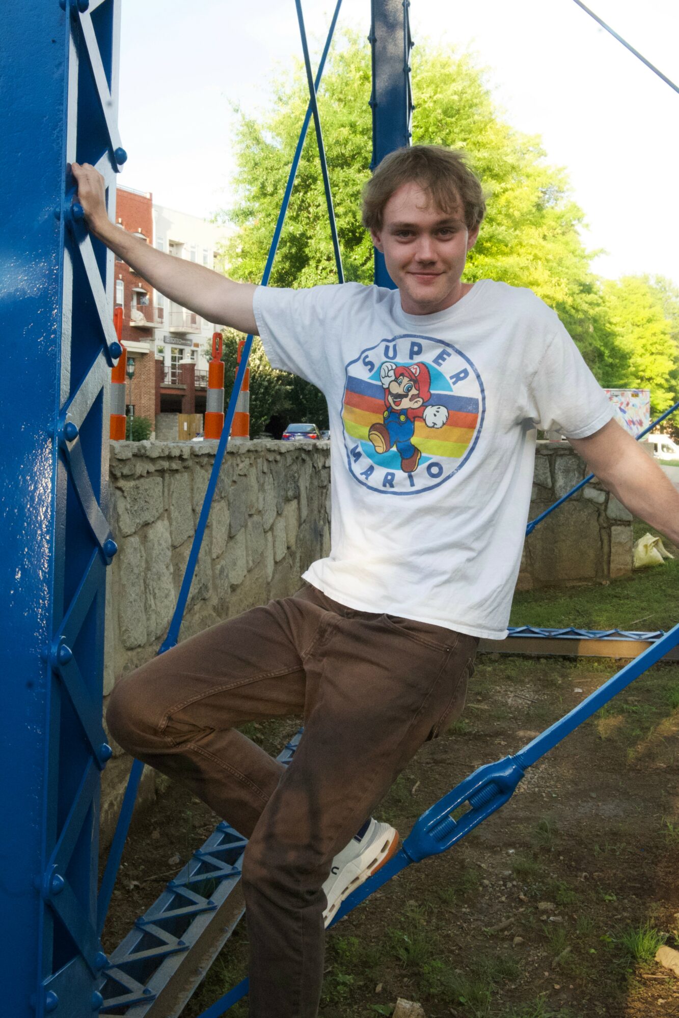 Young person sitting on a swing outdoors, smiling, with trees and a playground in the background.