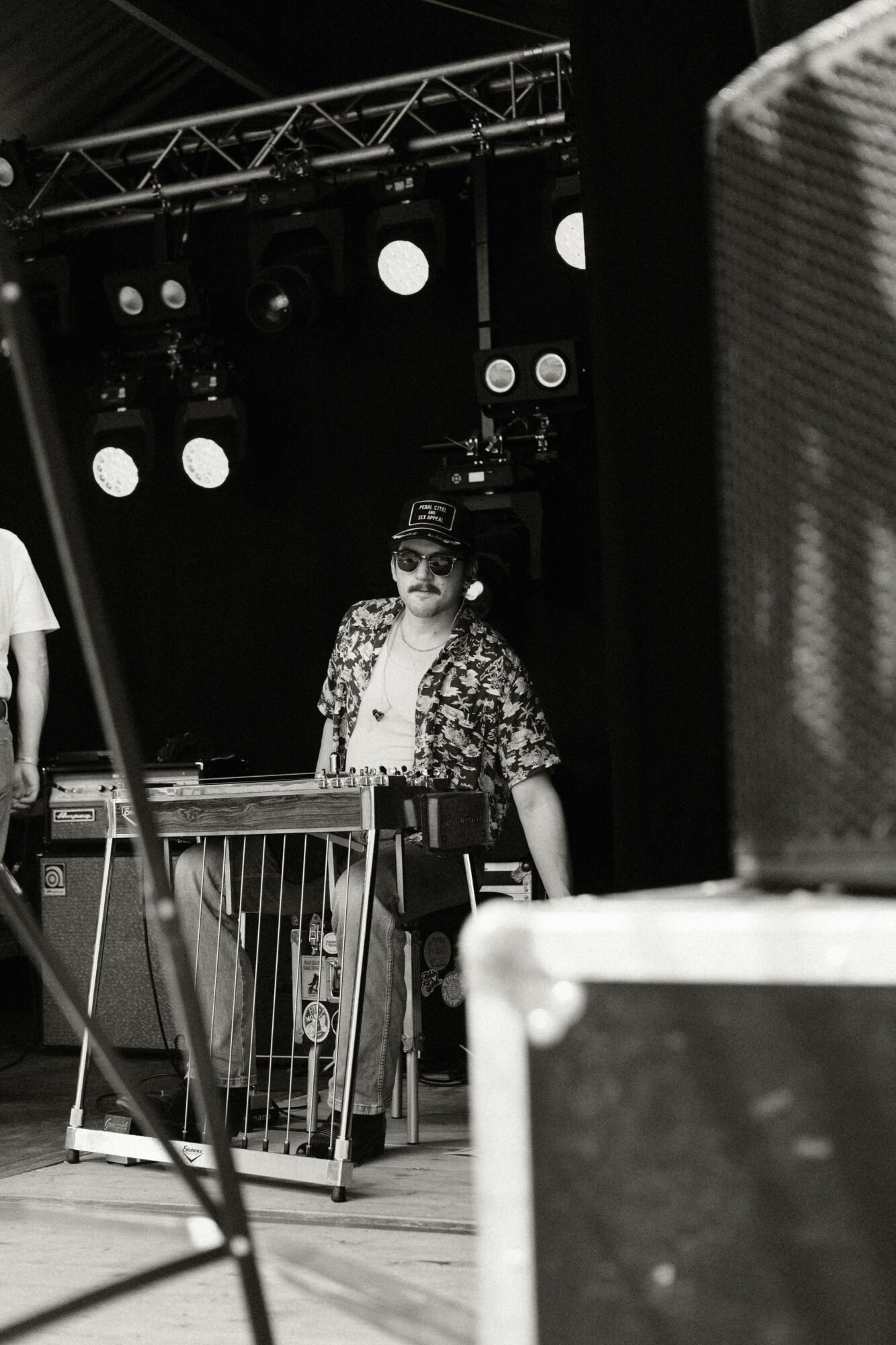 Person standing on stage with a microphone, stage lights, and equipment in the background.