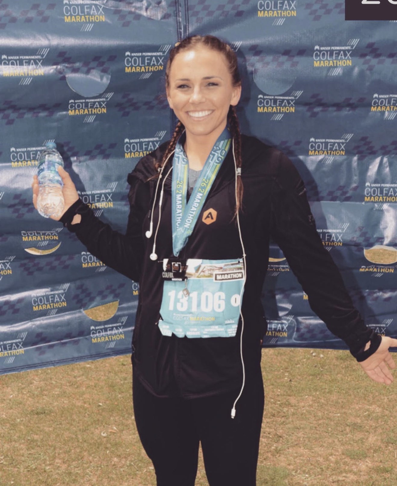 Smiling woman with medals and race bib, standing in front of a blue backdrop at a marathon event.