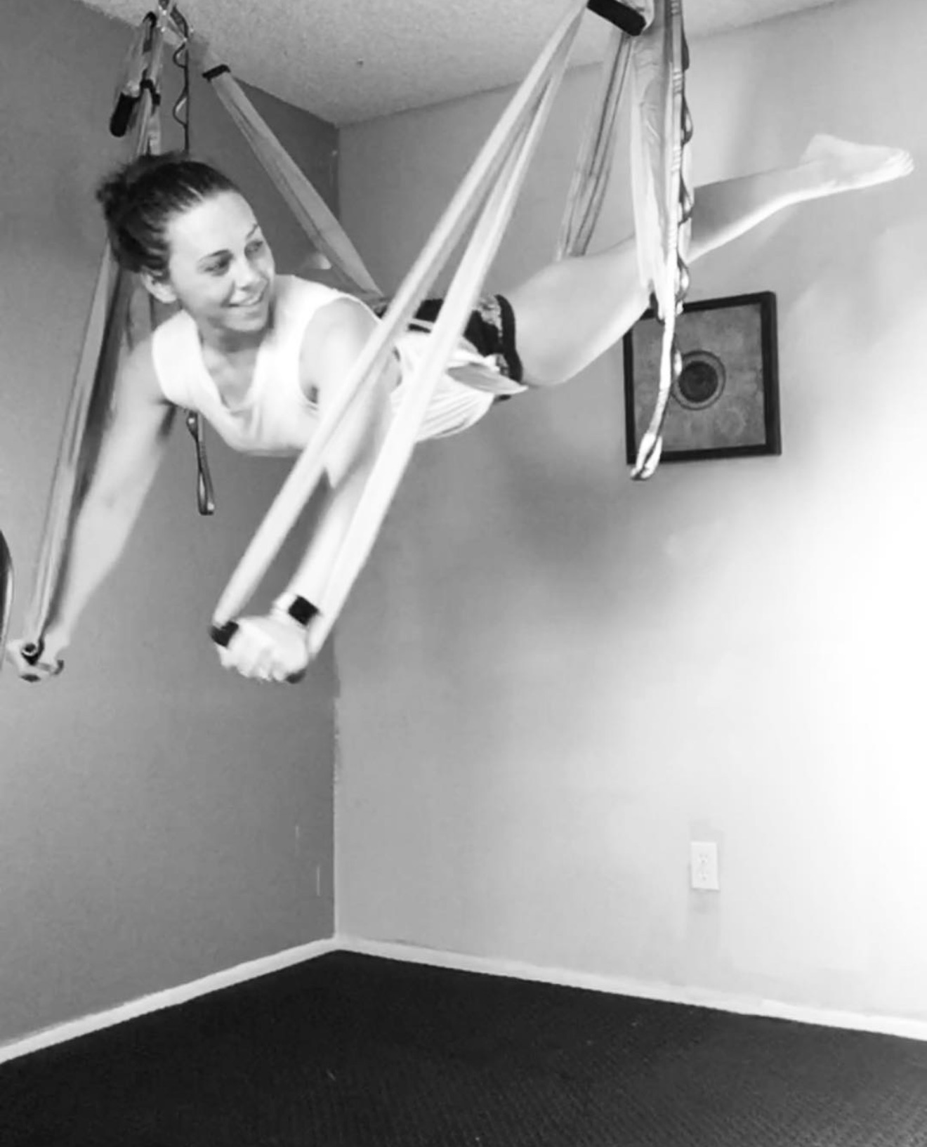Person hanging in a harness in a room with plain walls and a speaker on the wall.