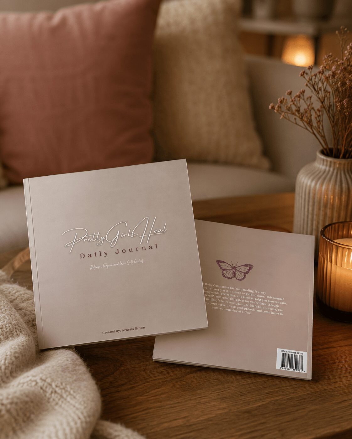Two notebooks on a wooden table, one with a butterfly illustration and text, the other with cursive writing, surrounded by candles and pillows.