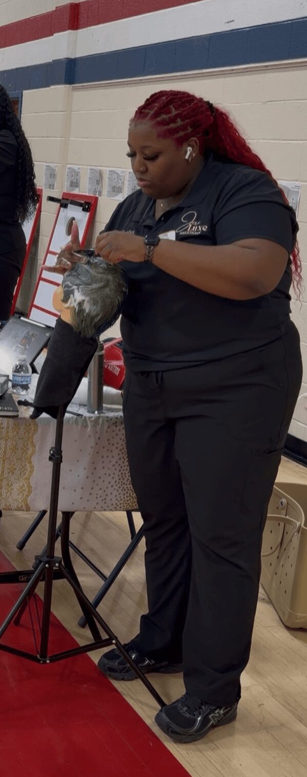 Person with red braided hair wearing a dark uniform, holding a fish, in a store or event setting.