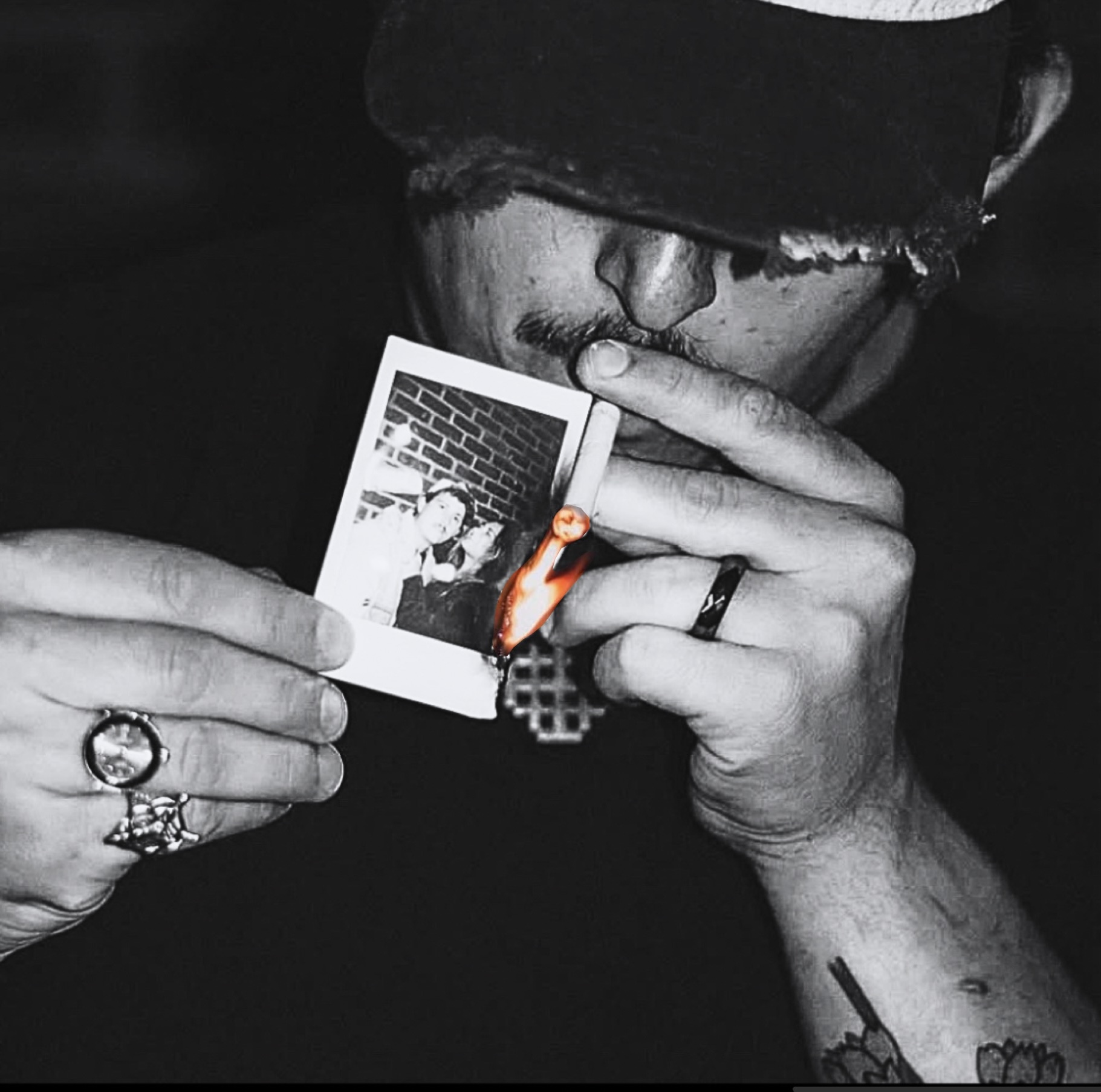Person wearing a hat and glasses holds a Polaroid photo close to their face, with rings on fingers and a tattoo visible on arm.