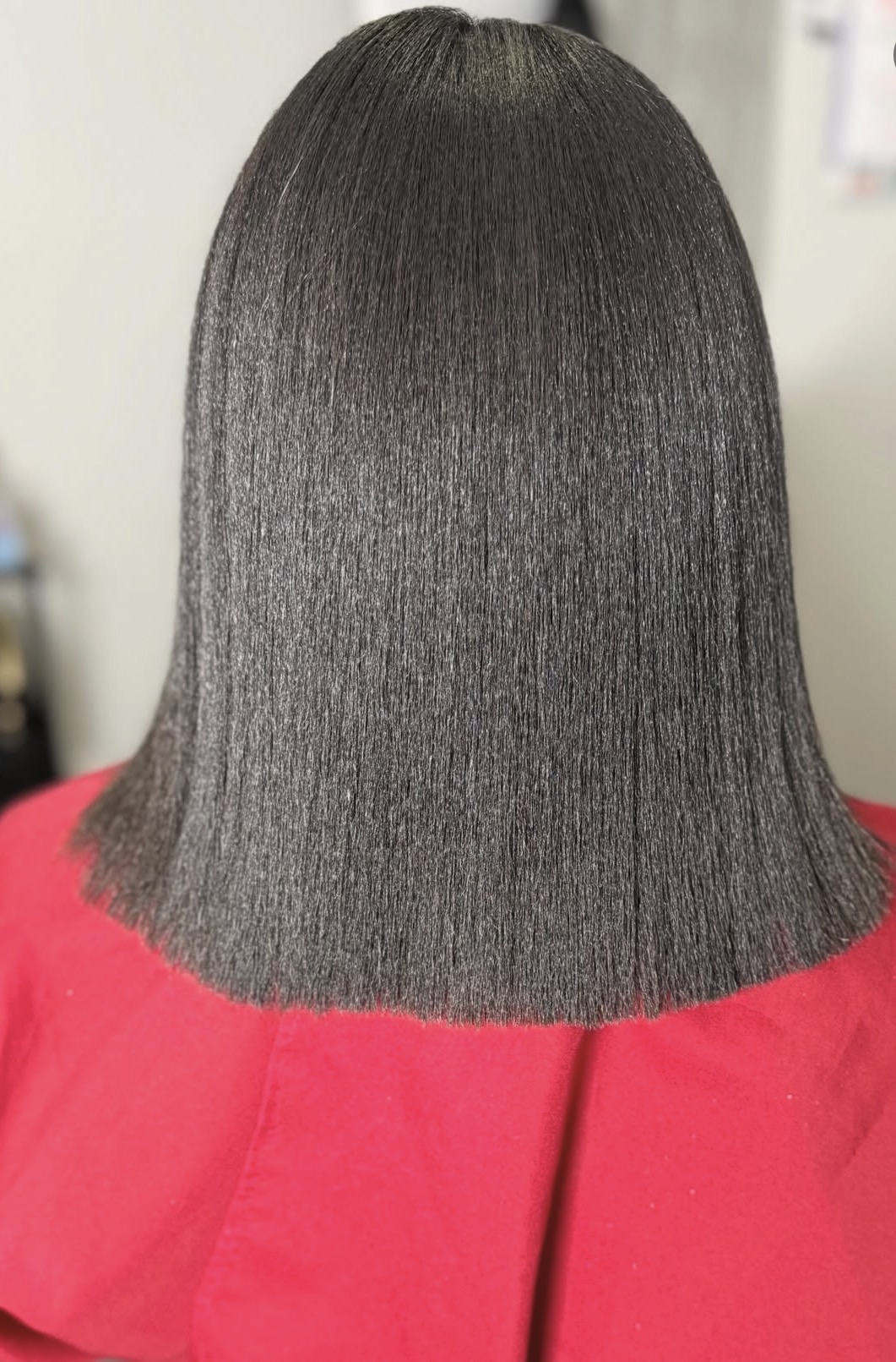 Back of a person with straight, shiny, shoulder-length dark hair wearing a red top.