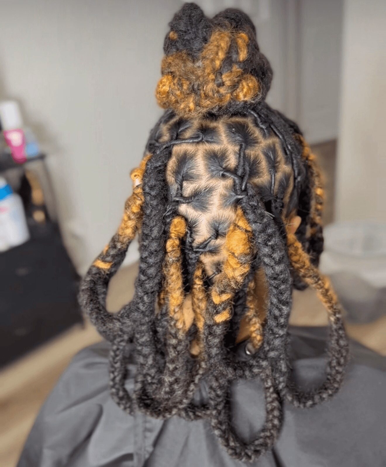 Back view of a person with styled dreadlocks, some with blonde highlights, tied up in a bun, with others hanging down.
