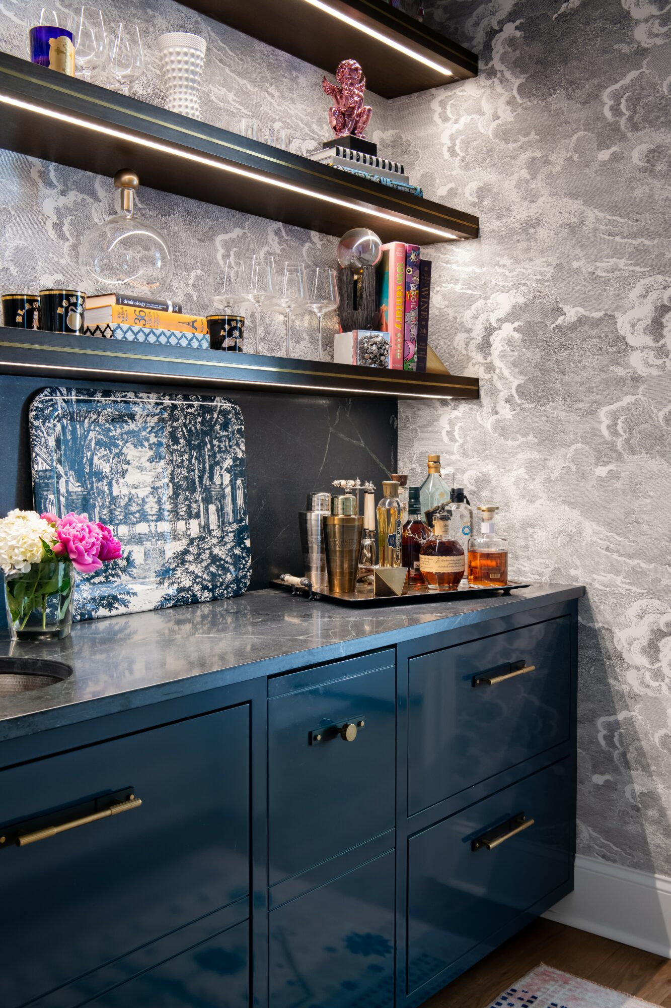 Blue cabinet with gold handles, marble countertop, shelves with books, decor, and flowers, textured gray wall background.