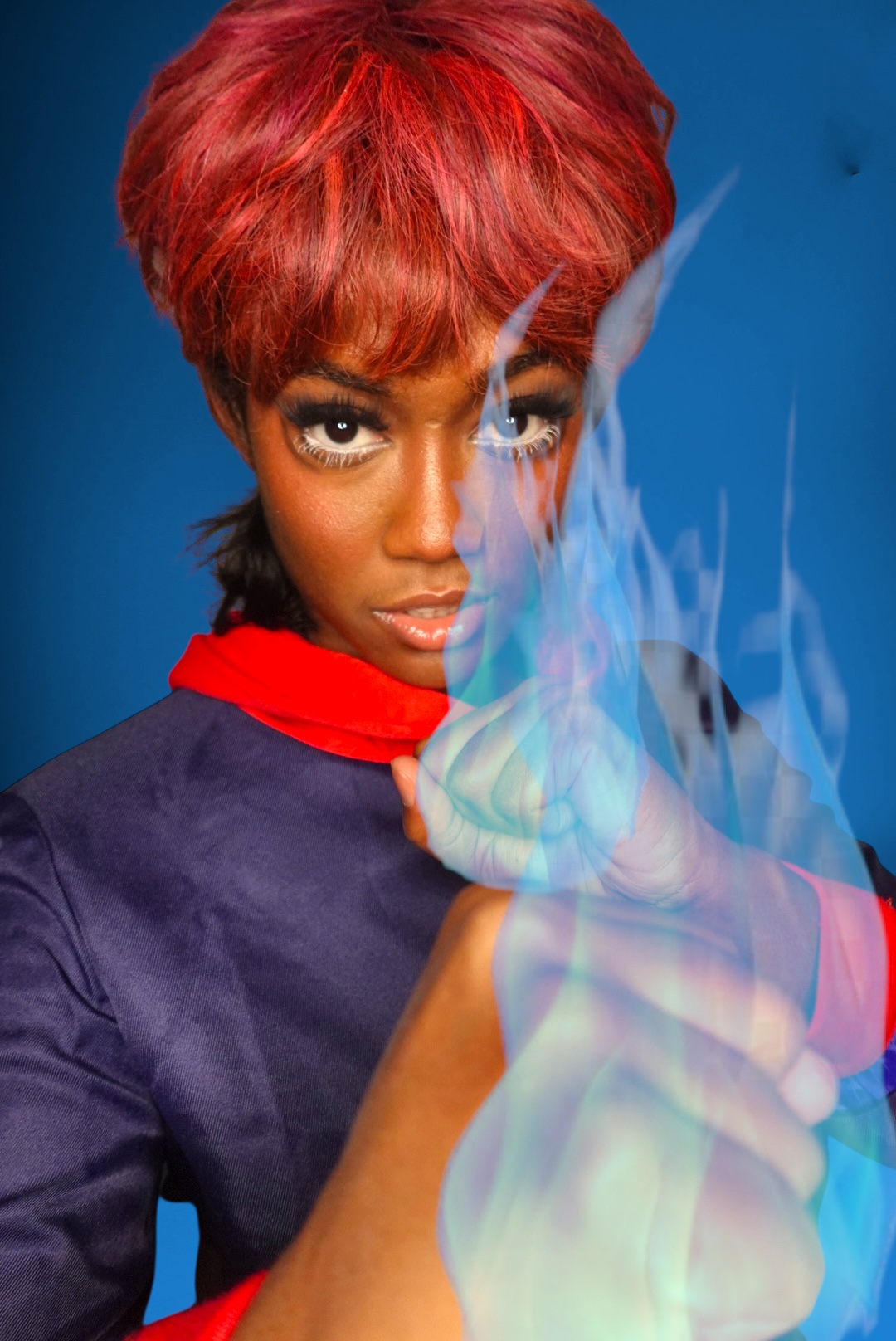Woman with red hair and intense gaze, holding a glowing object with blue smoke, against a blue background.
