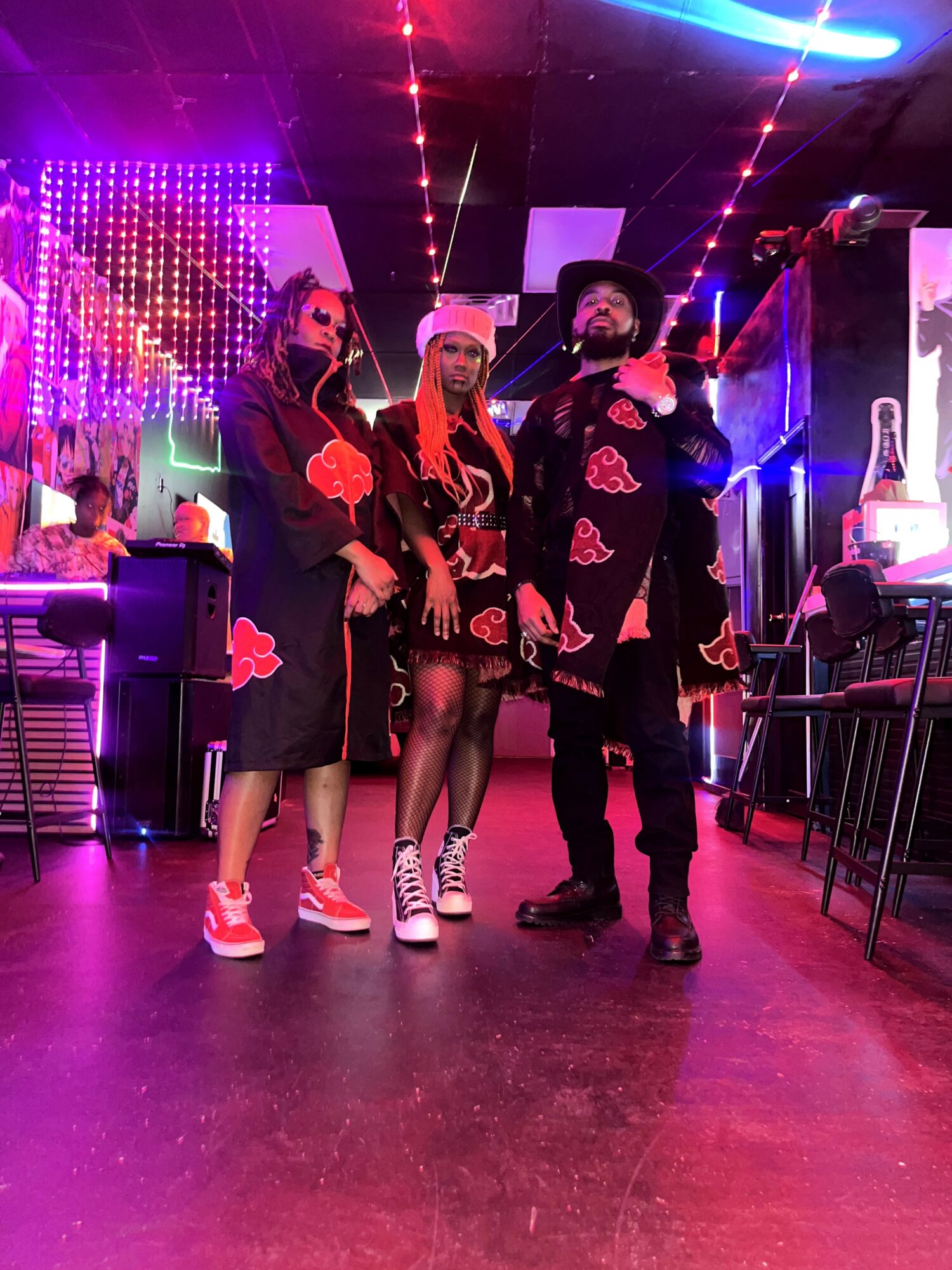 Four people in themed costumes stand in a colorful, neon-lit indoor setting with tables and chairs.