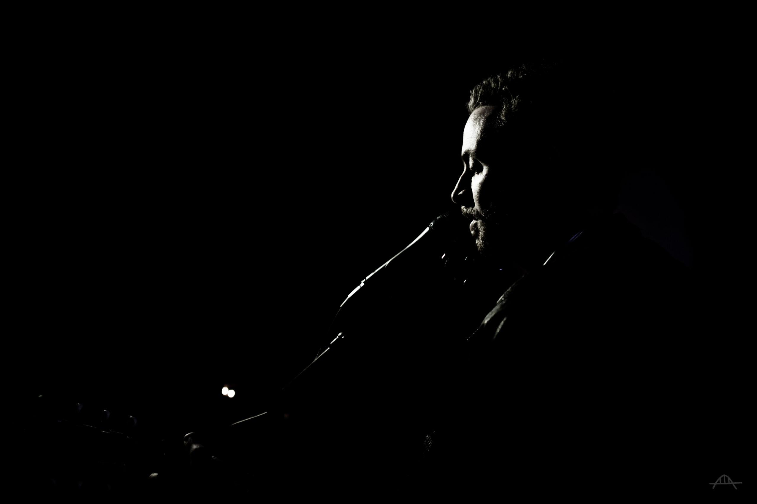 Person with face partially visible in low light, dark background, side profile, serious expression.