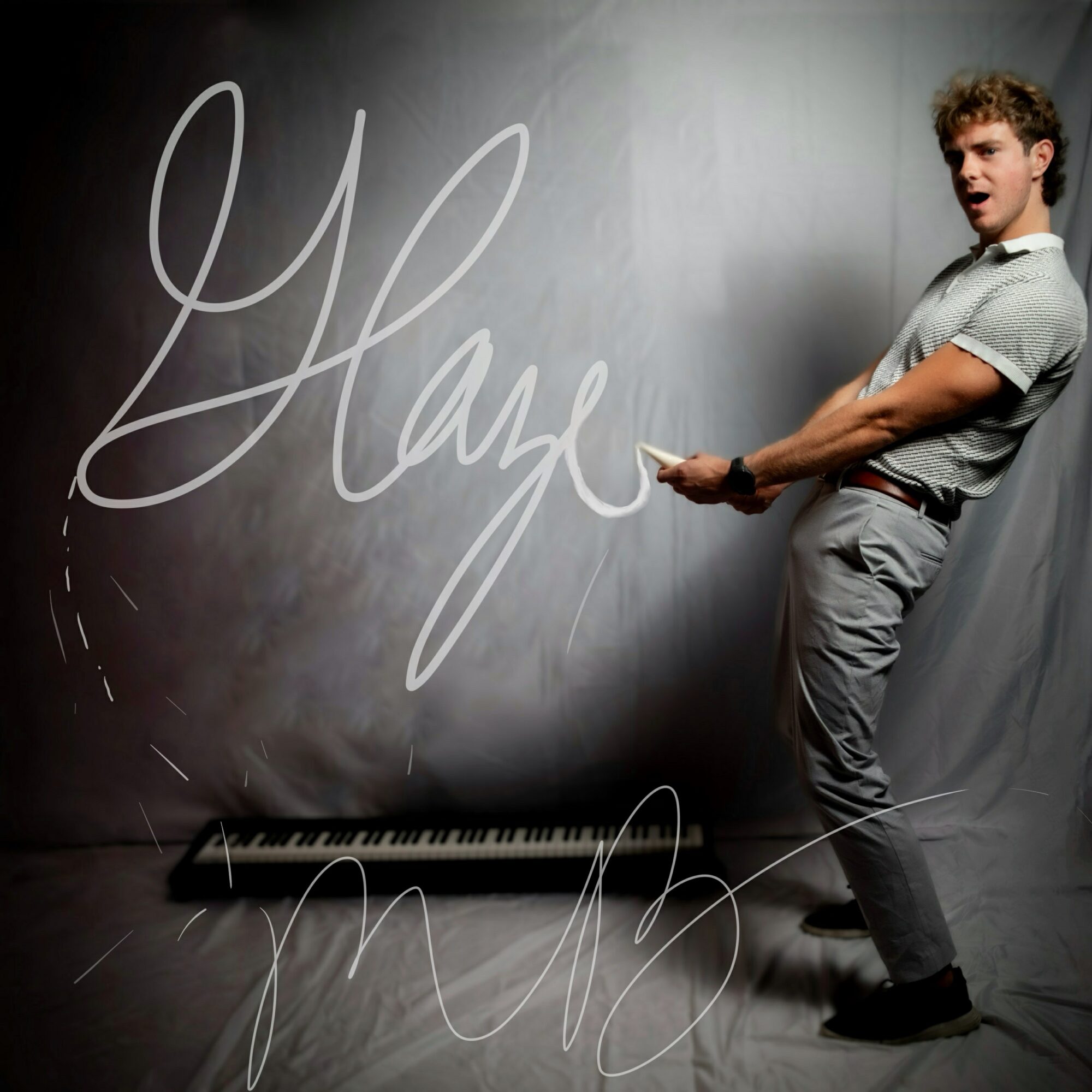 Young man standing next to a blackboard with the word 'Hype' written in large cursive, holding a marker, smiling.