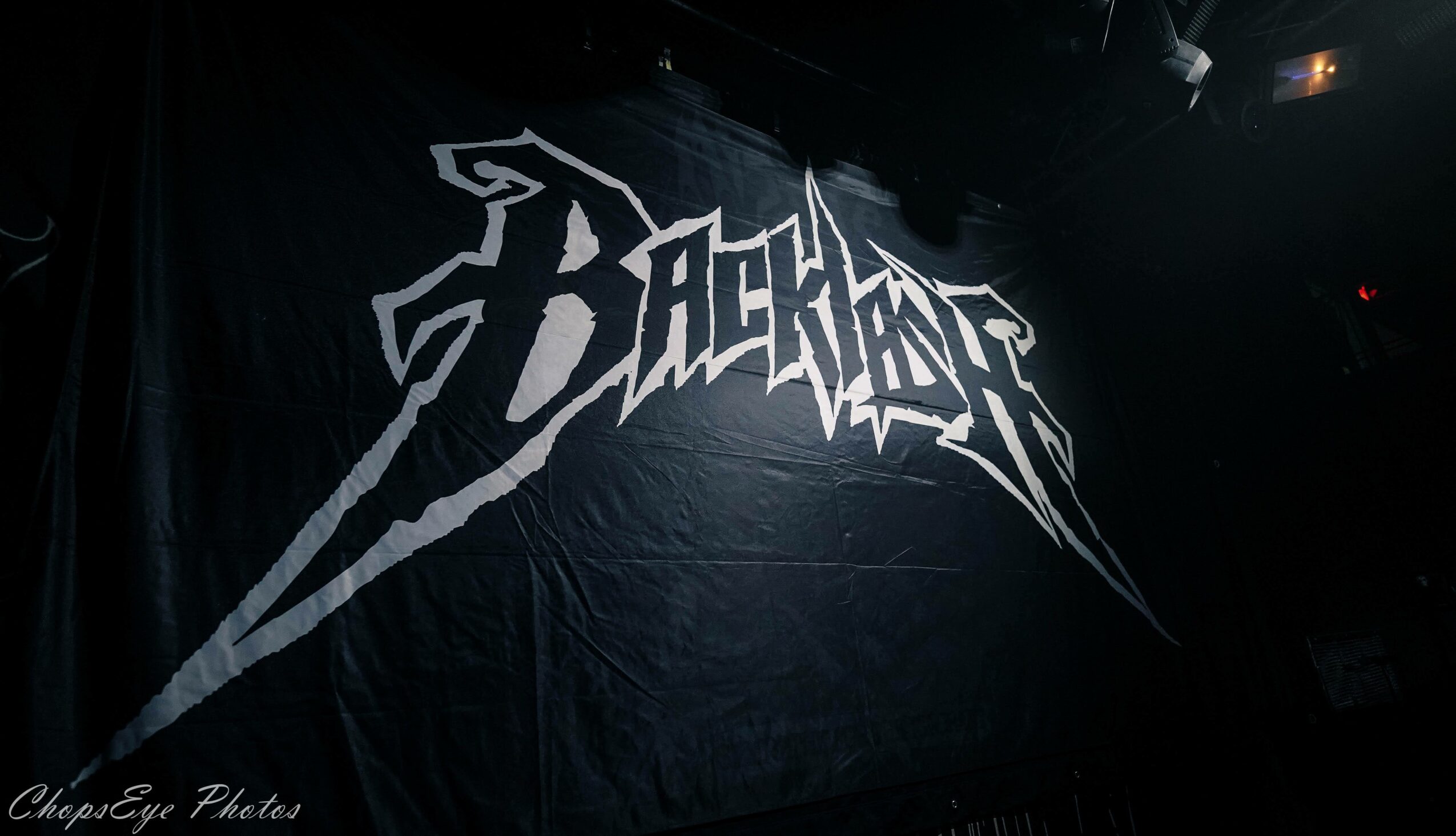 Black fabric with a white jagged logo reading 'Blackout' in stylized text, hanging in a dark setting.