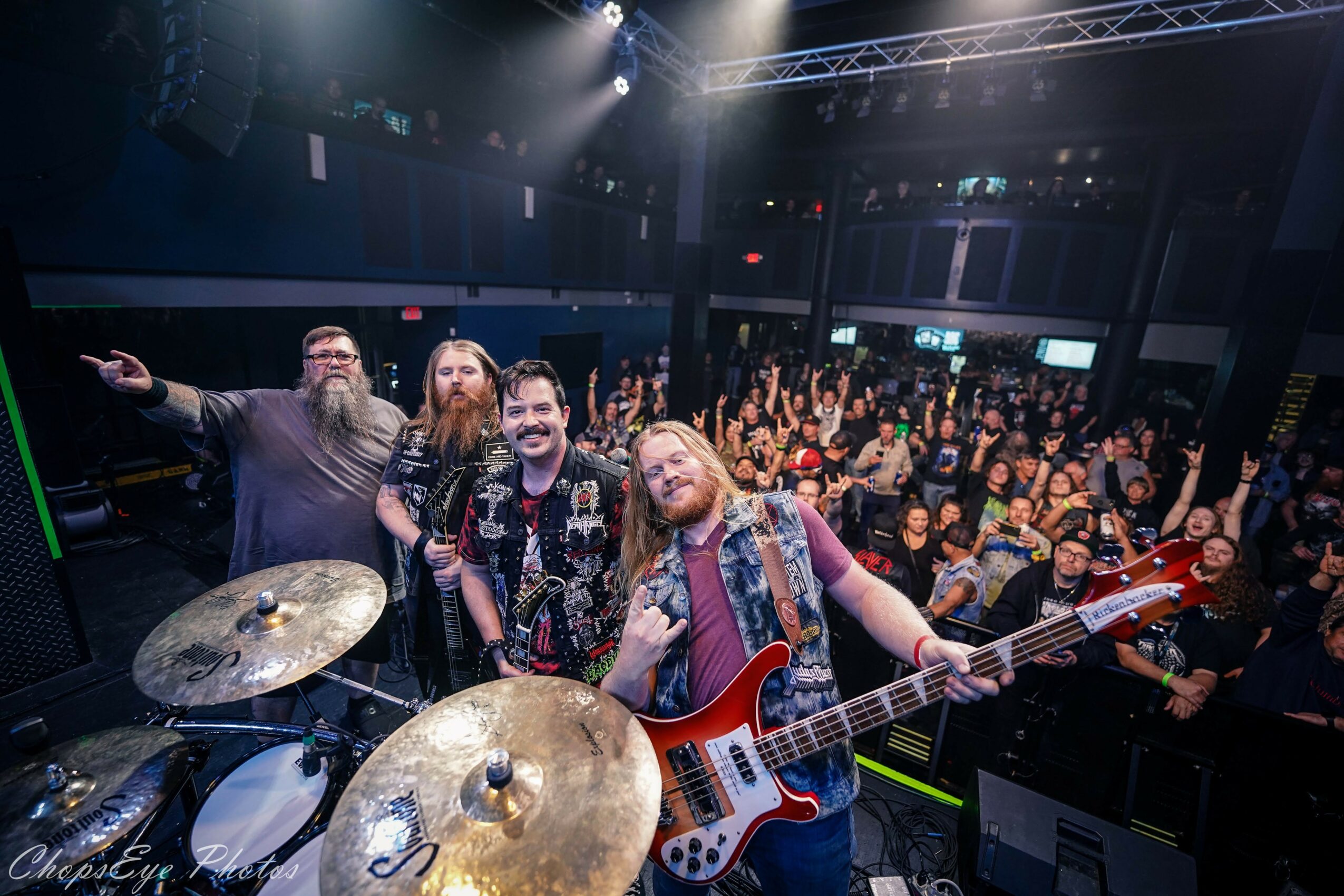 Band performing on stage with audience in the background, stage lights shining down, and band members smiling.