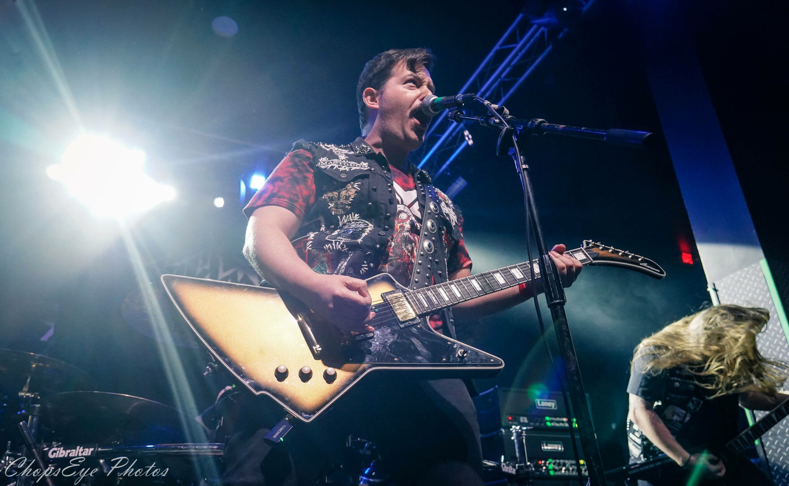 Person playing an electric guitar and singing into a microphone on stage with bright lights.