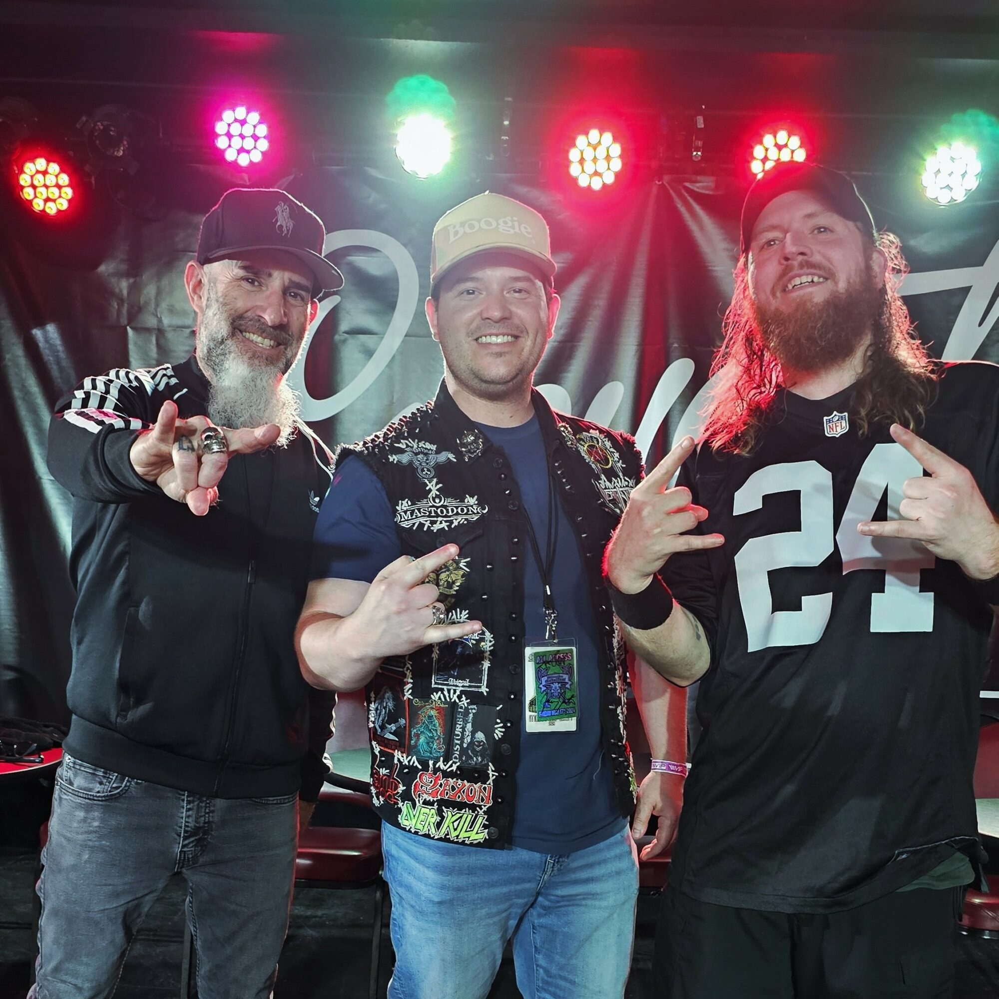 Three men smiling and posing on stage with colorful lights behind them.