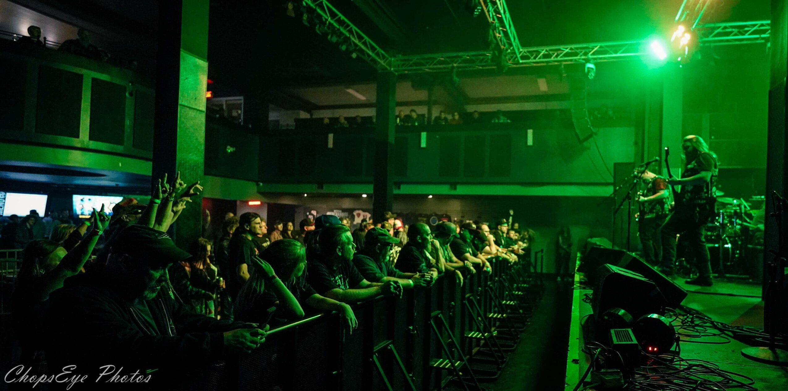 Audience watching a live music performance with green stage lighting, in a dark indoor venue, with a musician on stage.